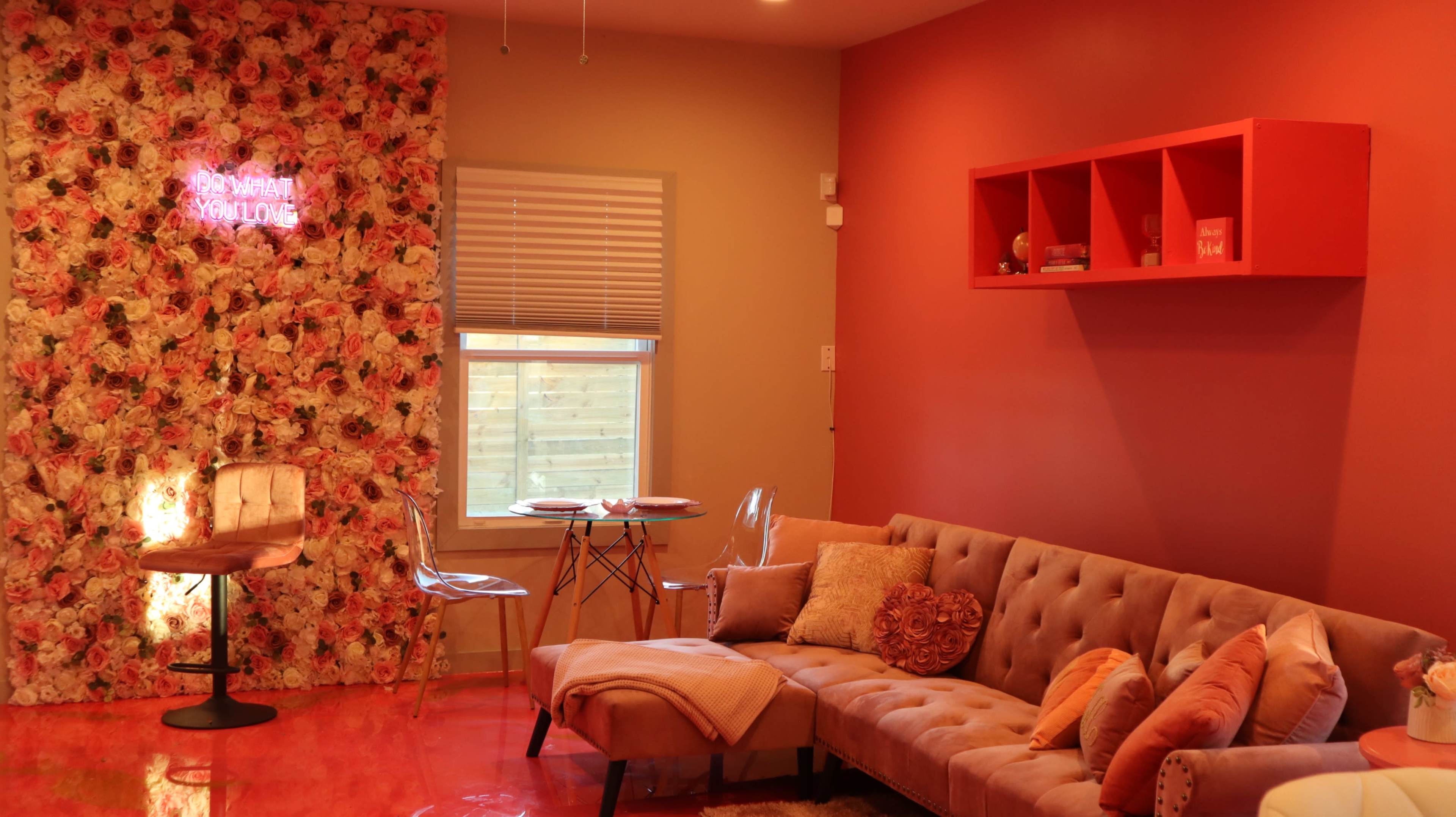 A cozy living room features a floral accent wall, a tan sectional sofa, and a small dining table with clear chairs.