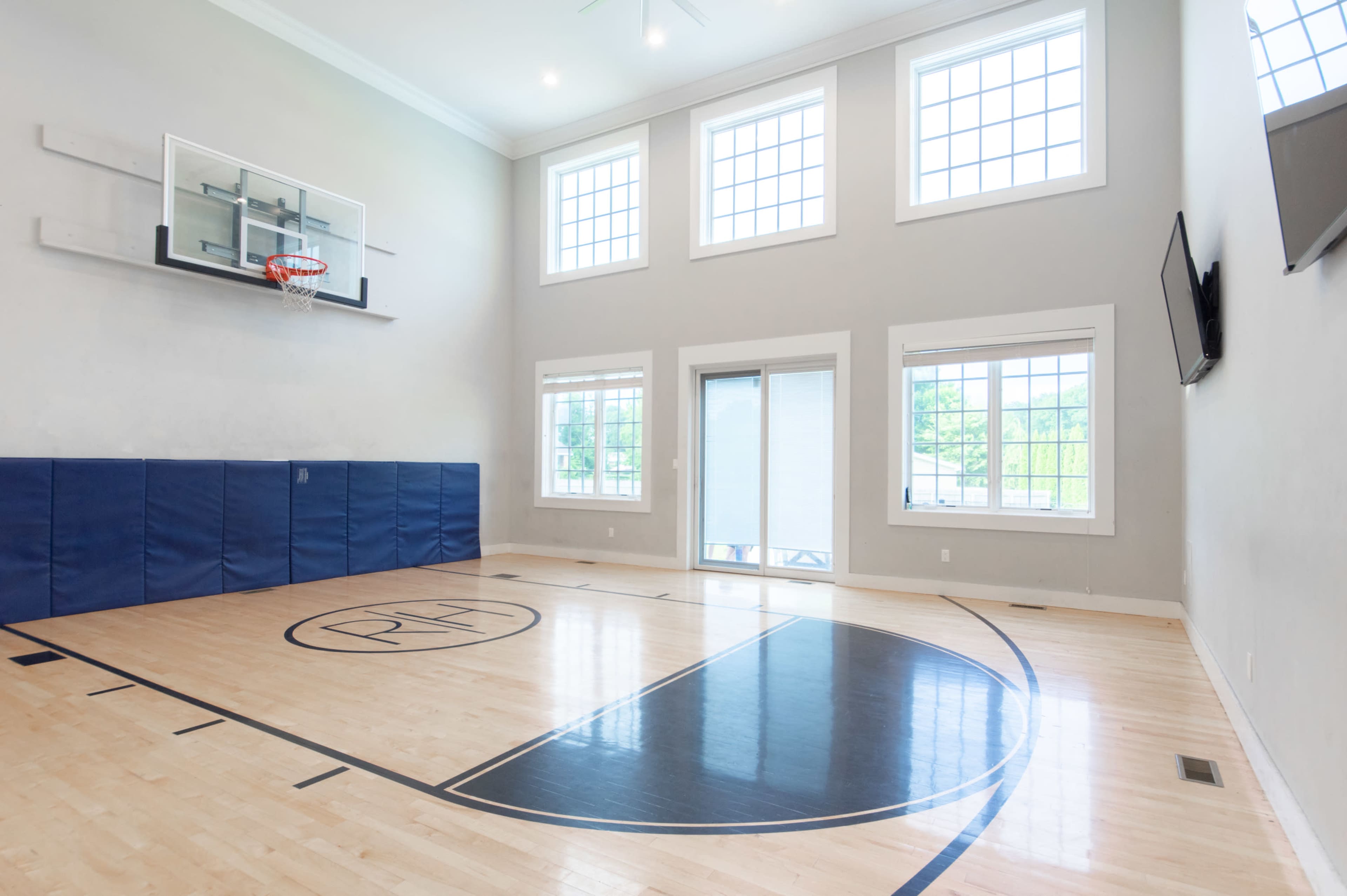 A well-lit indoor basketball court with a hoop, wooden flooring, and large windows.