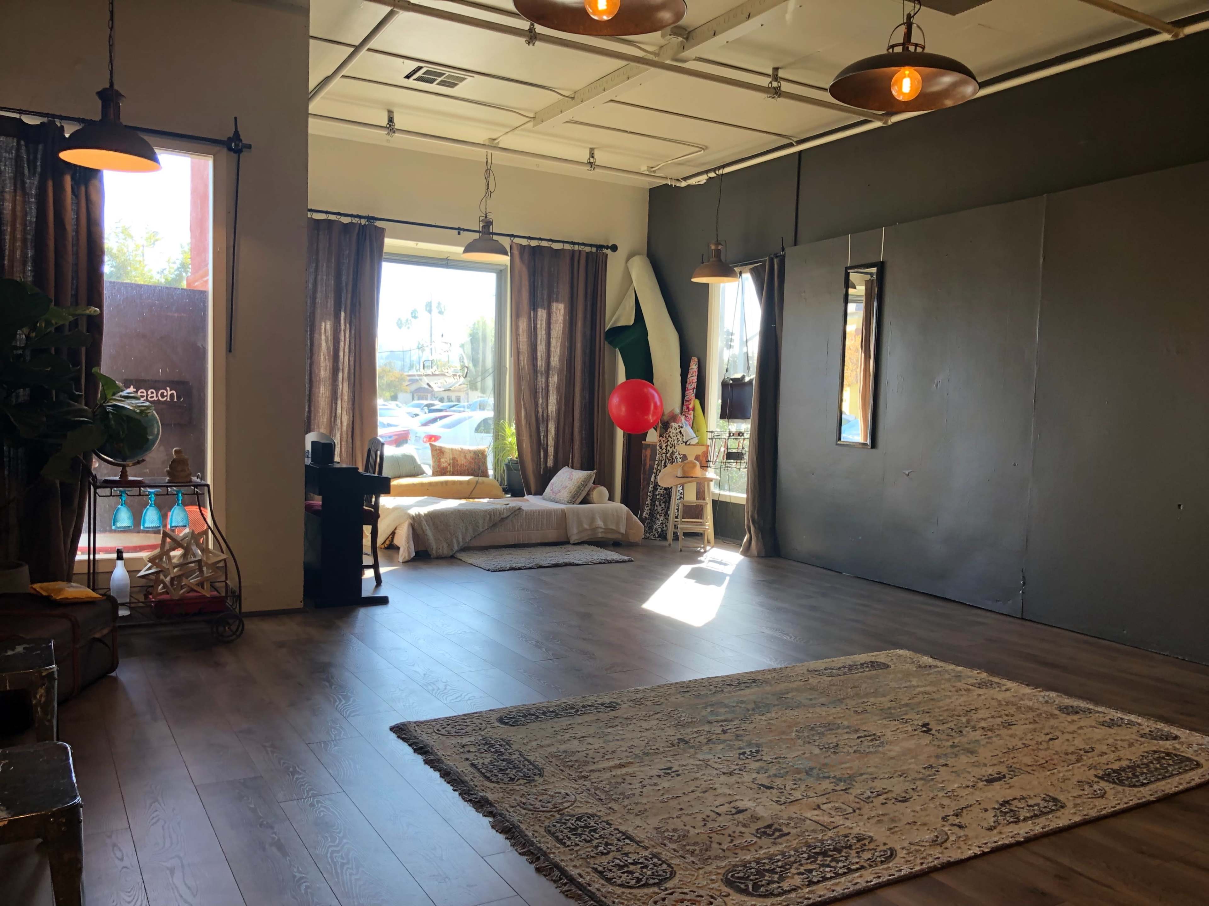 A spacious room with wooden flooring, large windows, and minimal furnishings, including a rug and a couch, and features a red balloon suspended in the air.