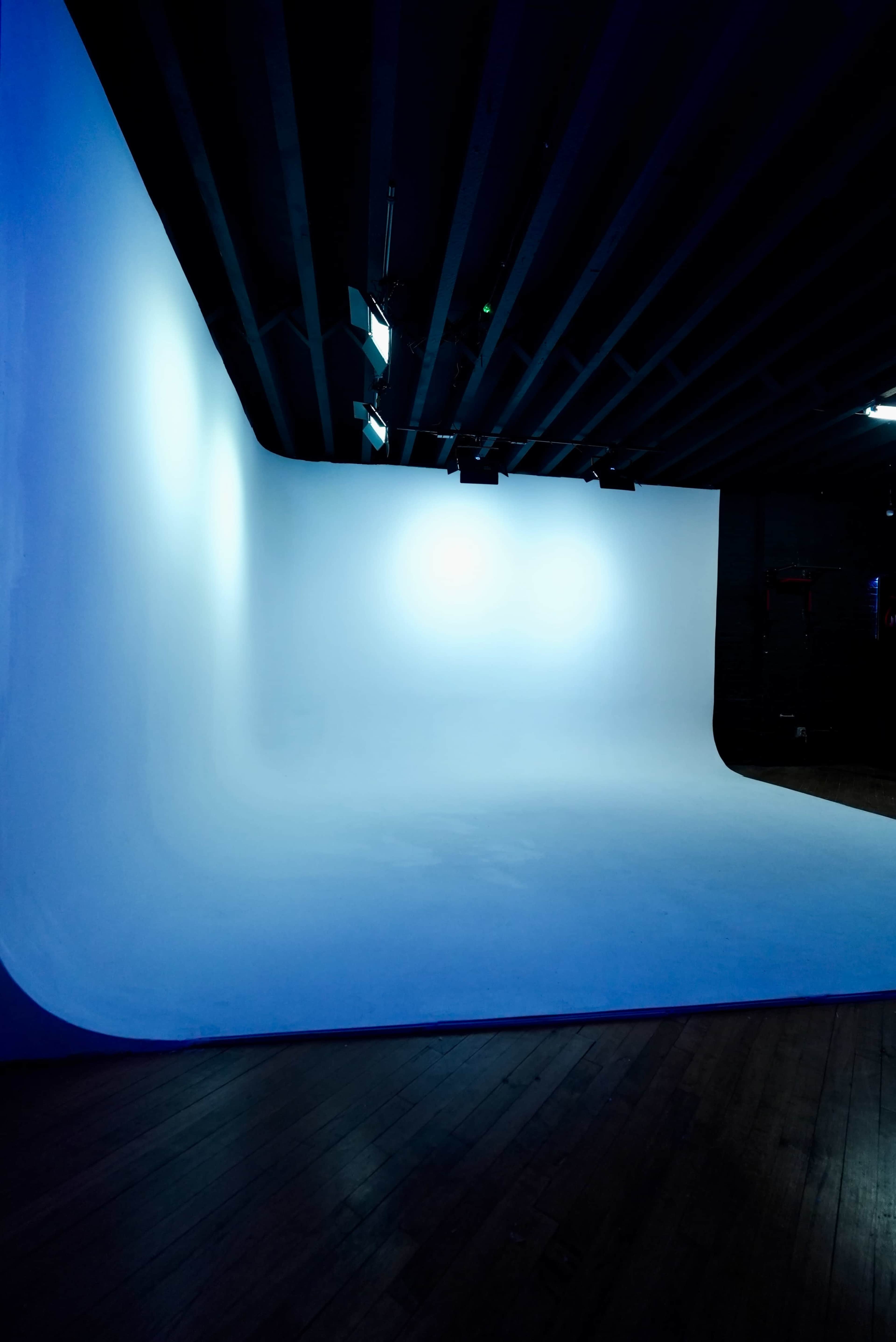 The image shows an empty studio with a smooth blue backdrop and overhead lighting.