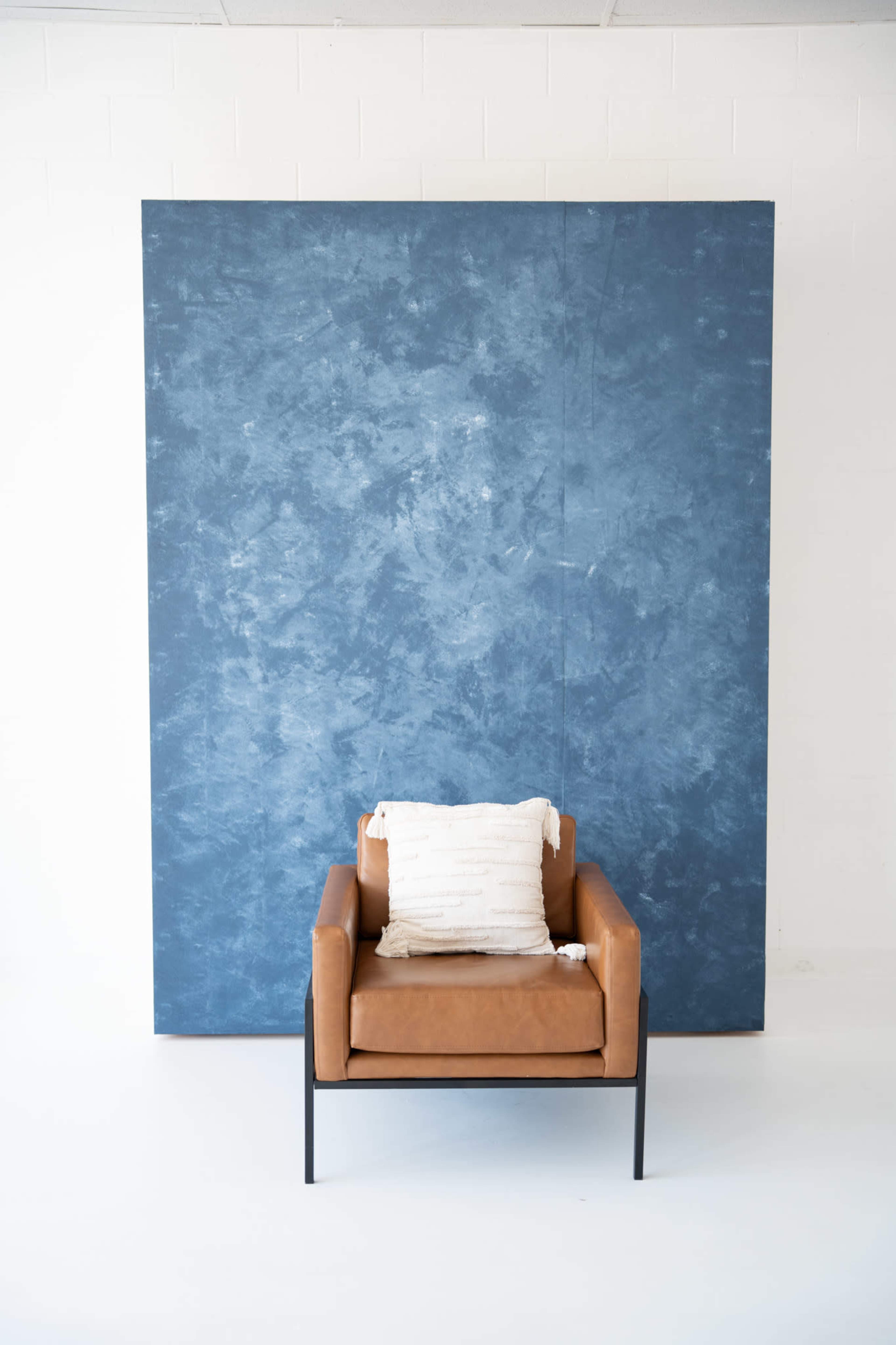 A brown leather armchair with a white decorative pillow is positioned in front of a textured blue backdrop.