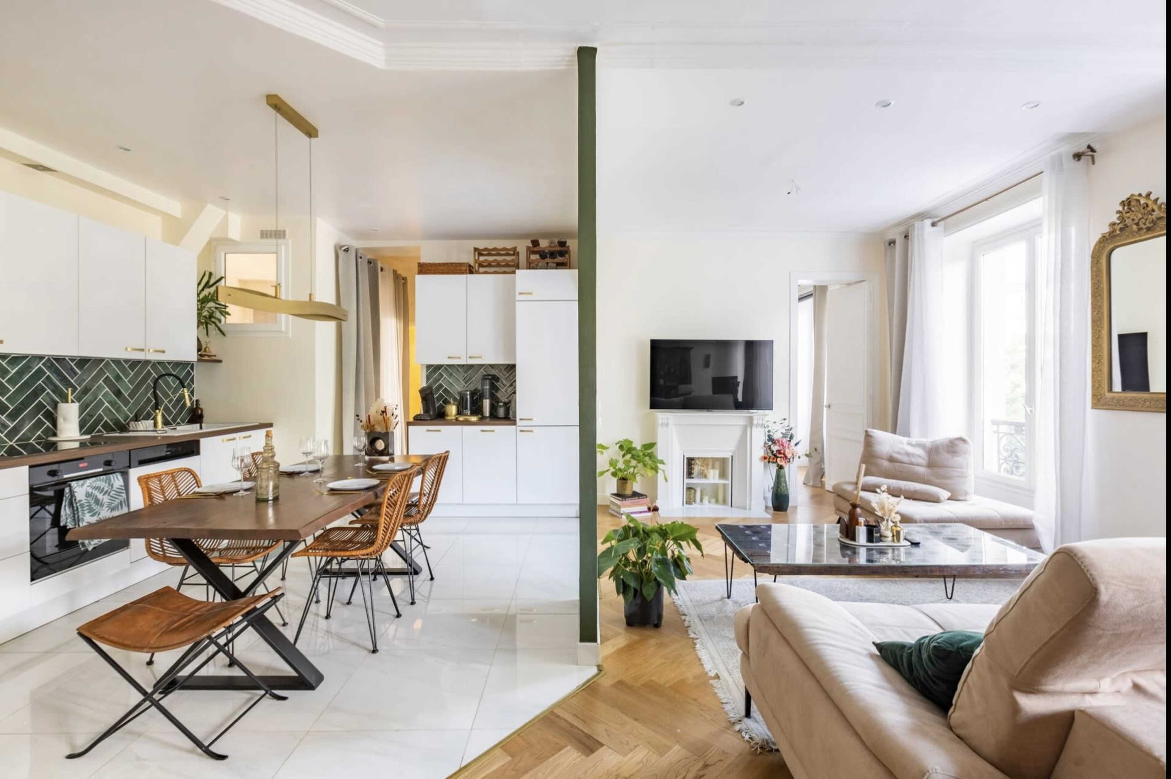 The image shows a modern, open-concept living space featuring a kitchen with a dining table on one side and a cozy lounge area with a sofa and television on the other.