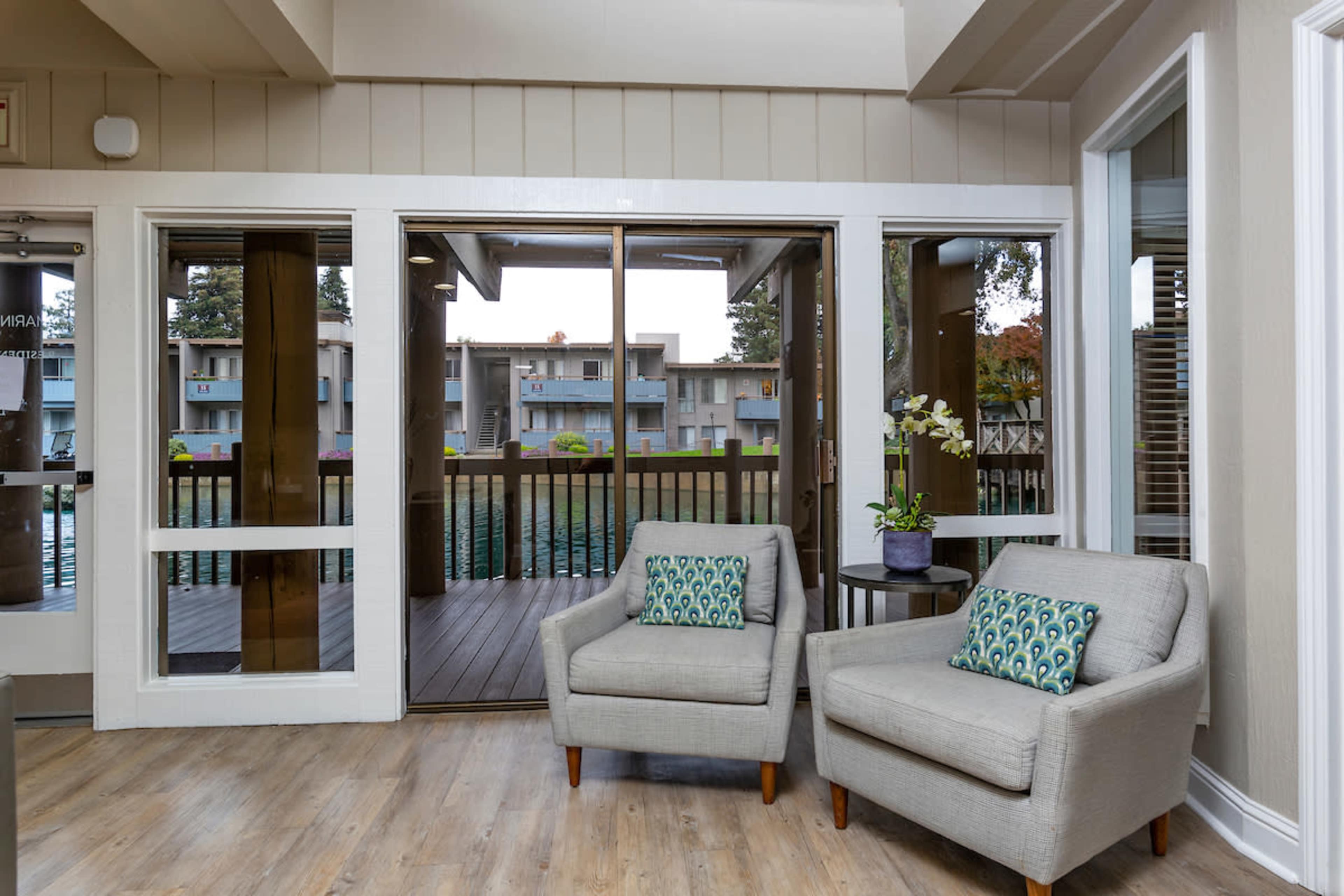 A cozy sitting area with two chairs and a small side table, overlooking a deck through large glass doors.