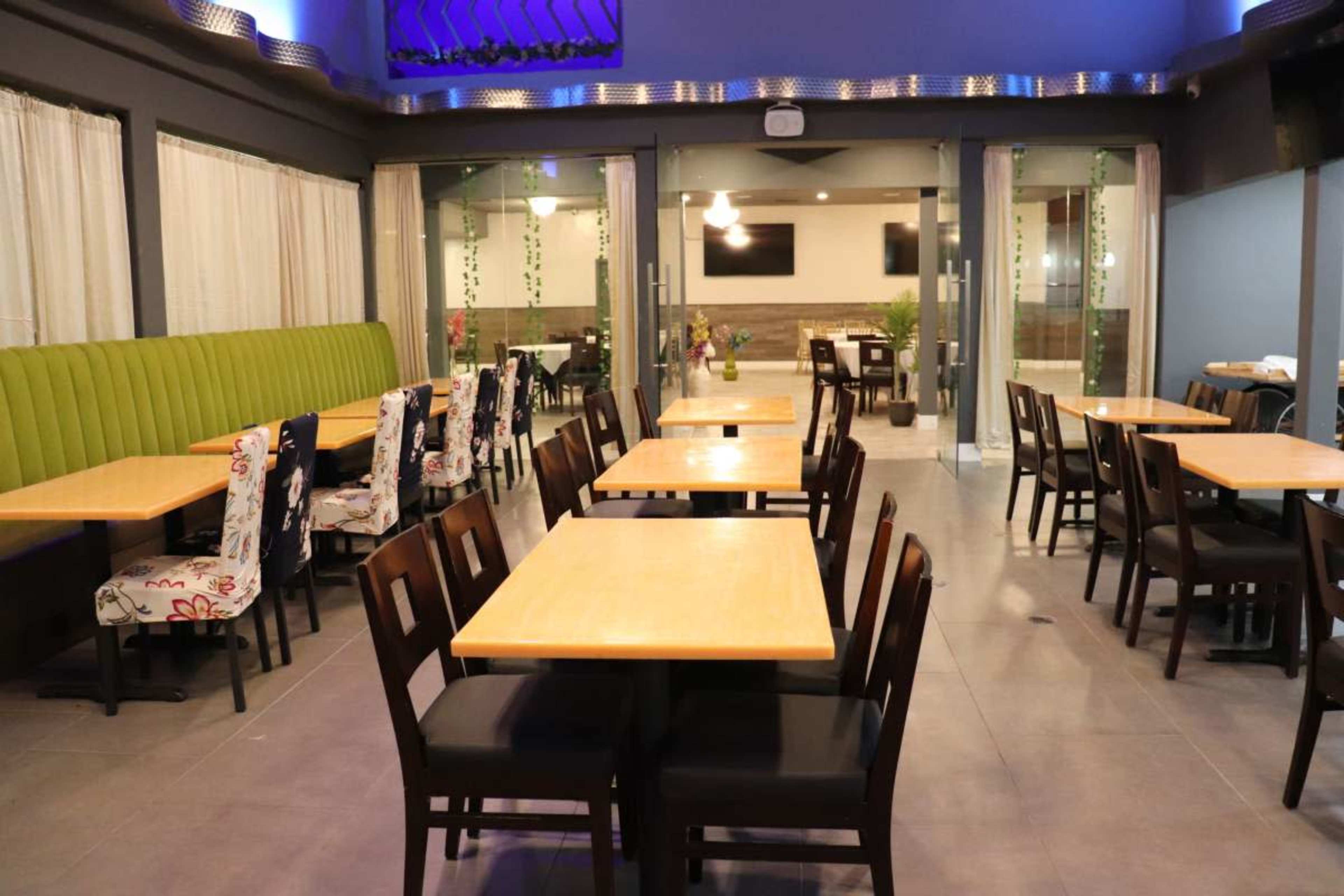 The image shows a restaurant interior with a mix of wooden tables and chairs, featuring a green banquette along one wall and a modern decor.