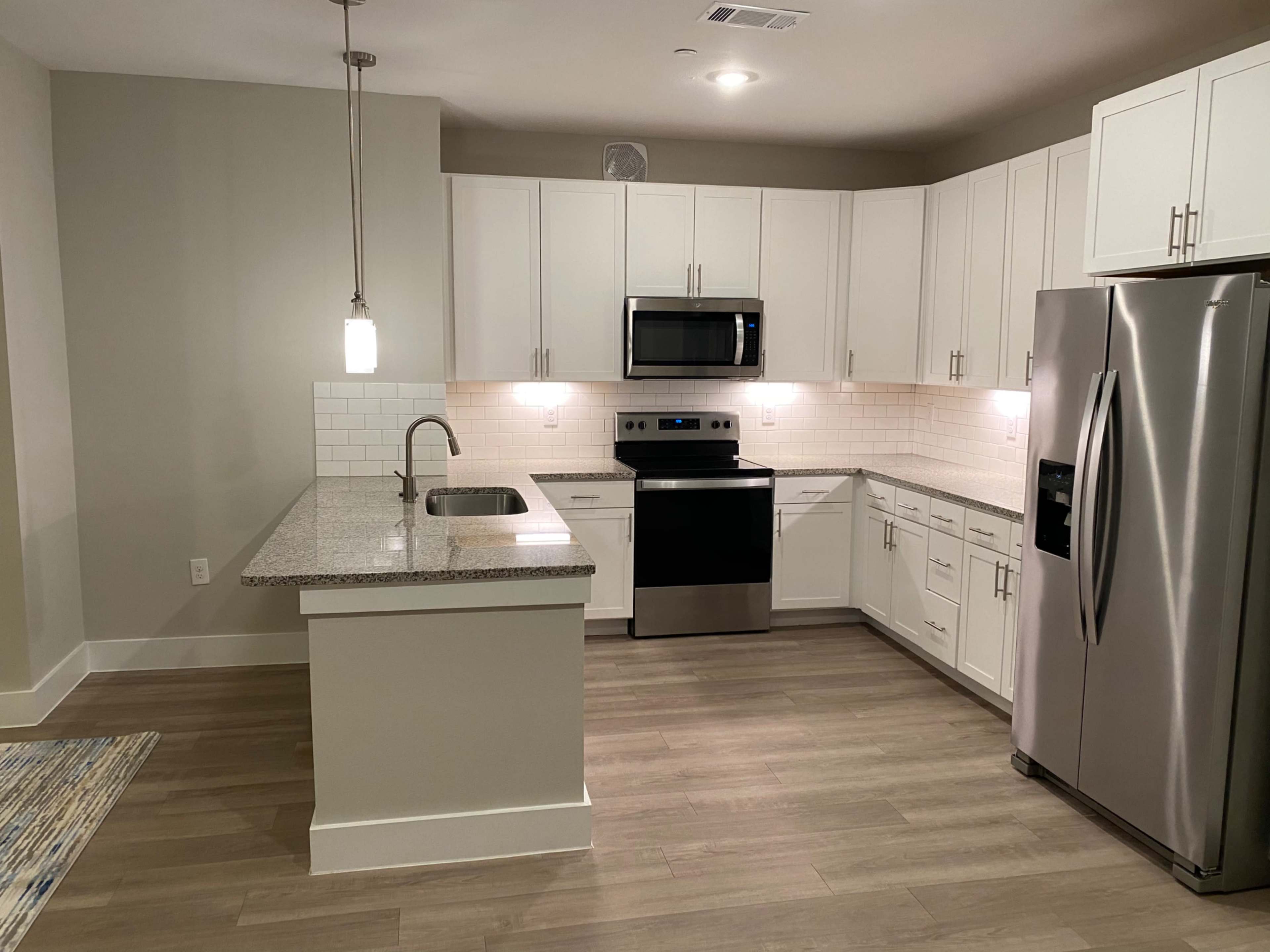 A modern kitchen with white cabinetry, stainless steel appliances, and a granite countertop island.