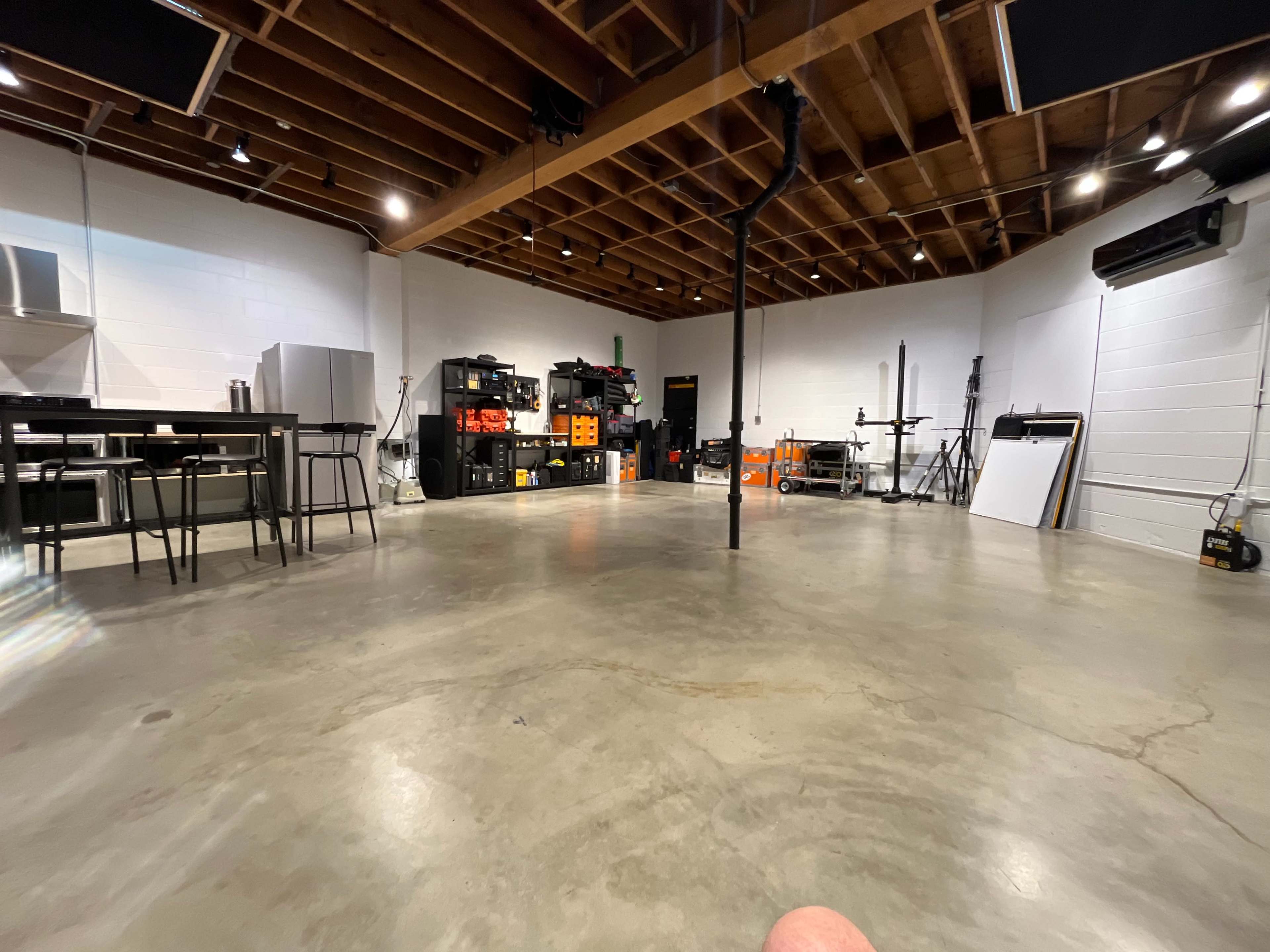 A spacious workshop with concrete flooring, various tools and equipment organized along the walls, and a table set up in the foreground.
