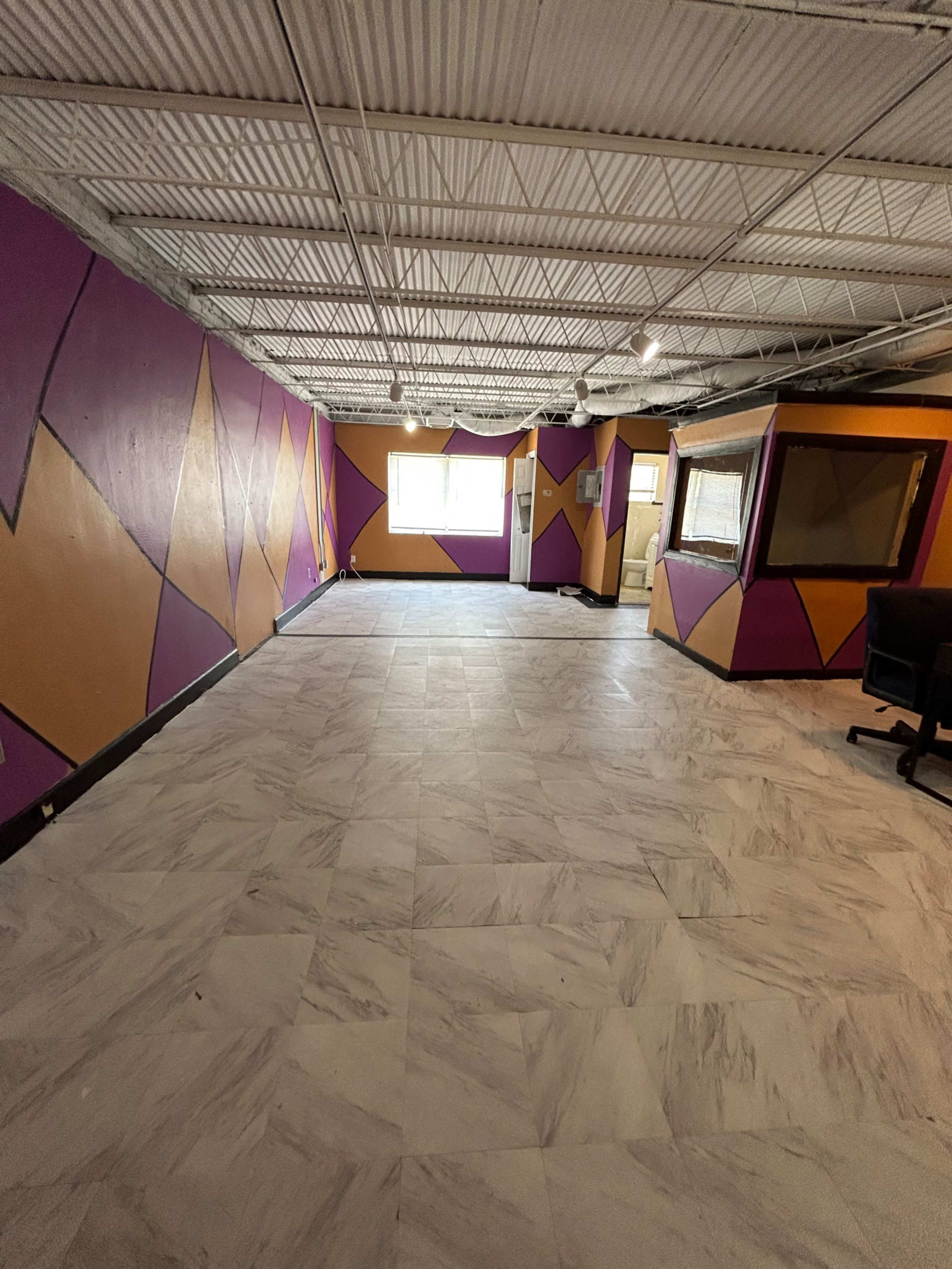 A spacious, partially finished room with geometric designs in purple and gold on the walls and marble flooring.