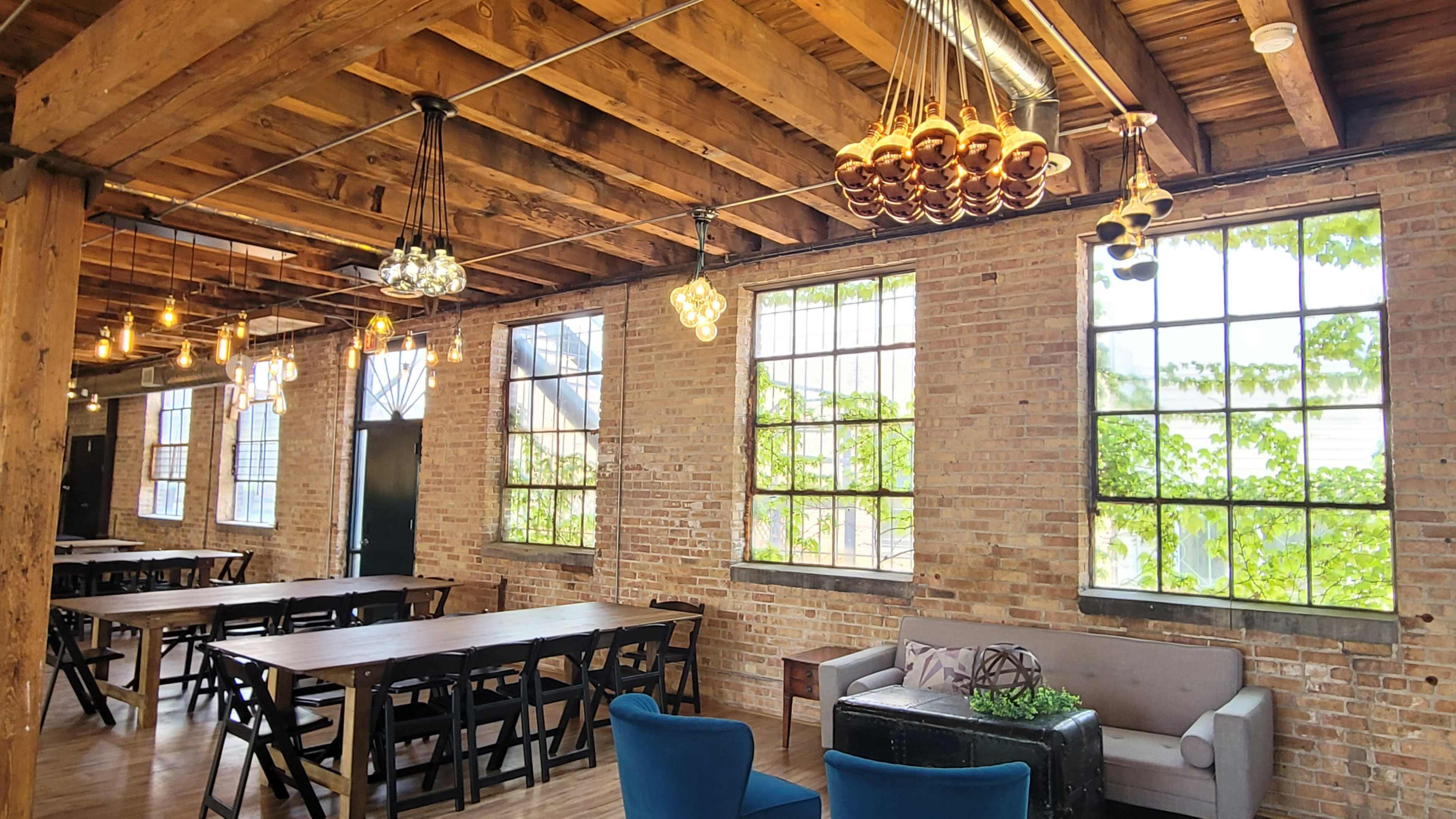 The image shows a spacious interior with wooden beams, large windows, and a mix of dining tables and seating areas.