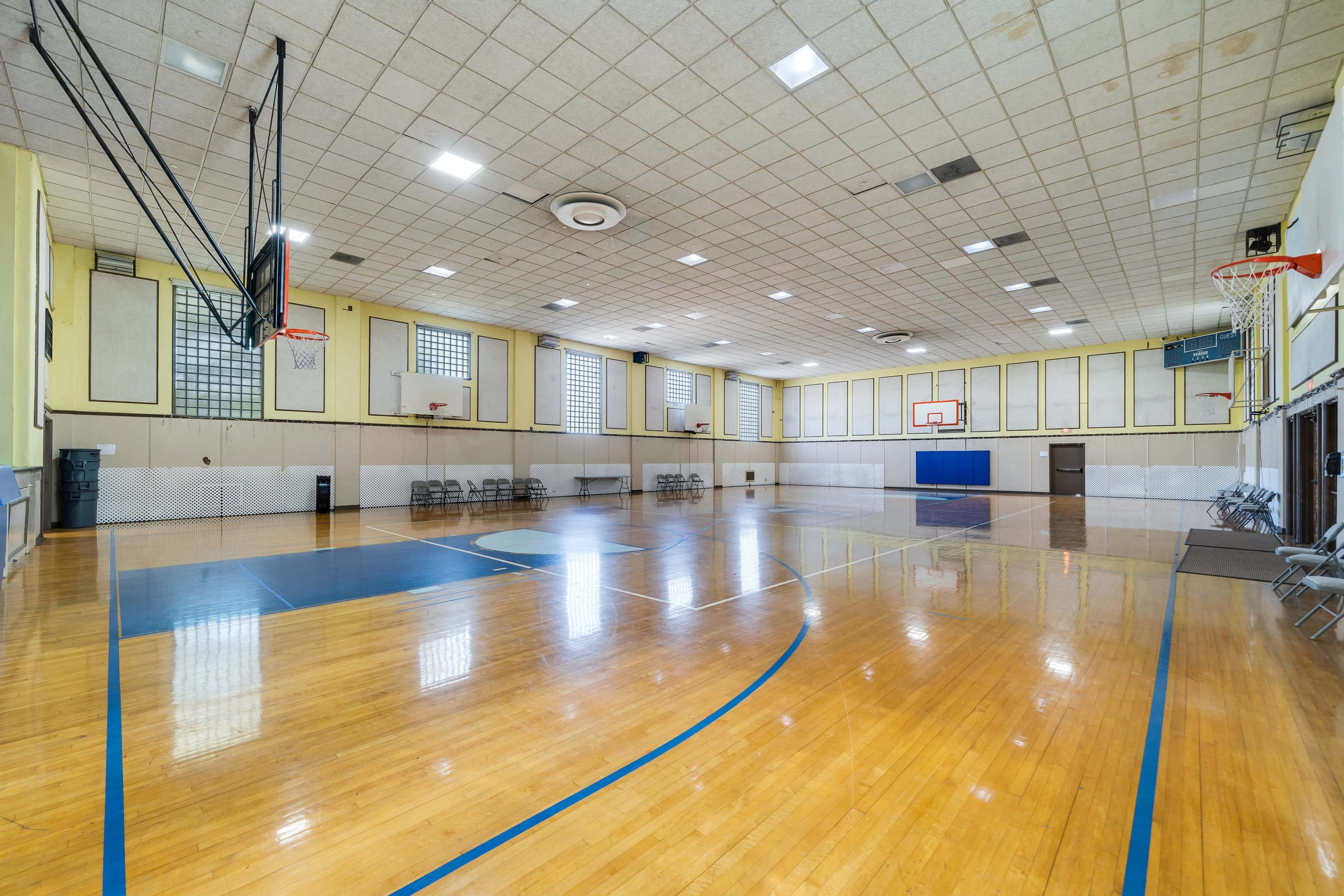 An empty gymnasium features wooden floors, basketball hoops, and rows of chairs along the walls.