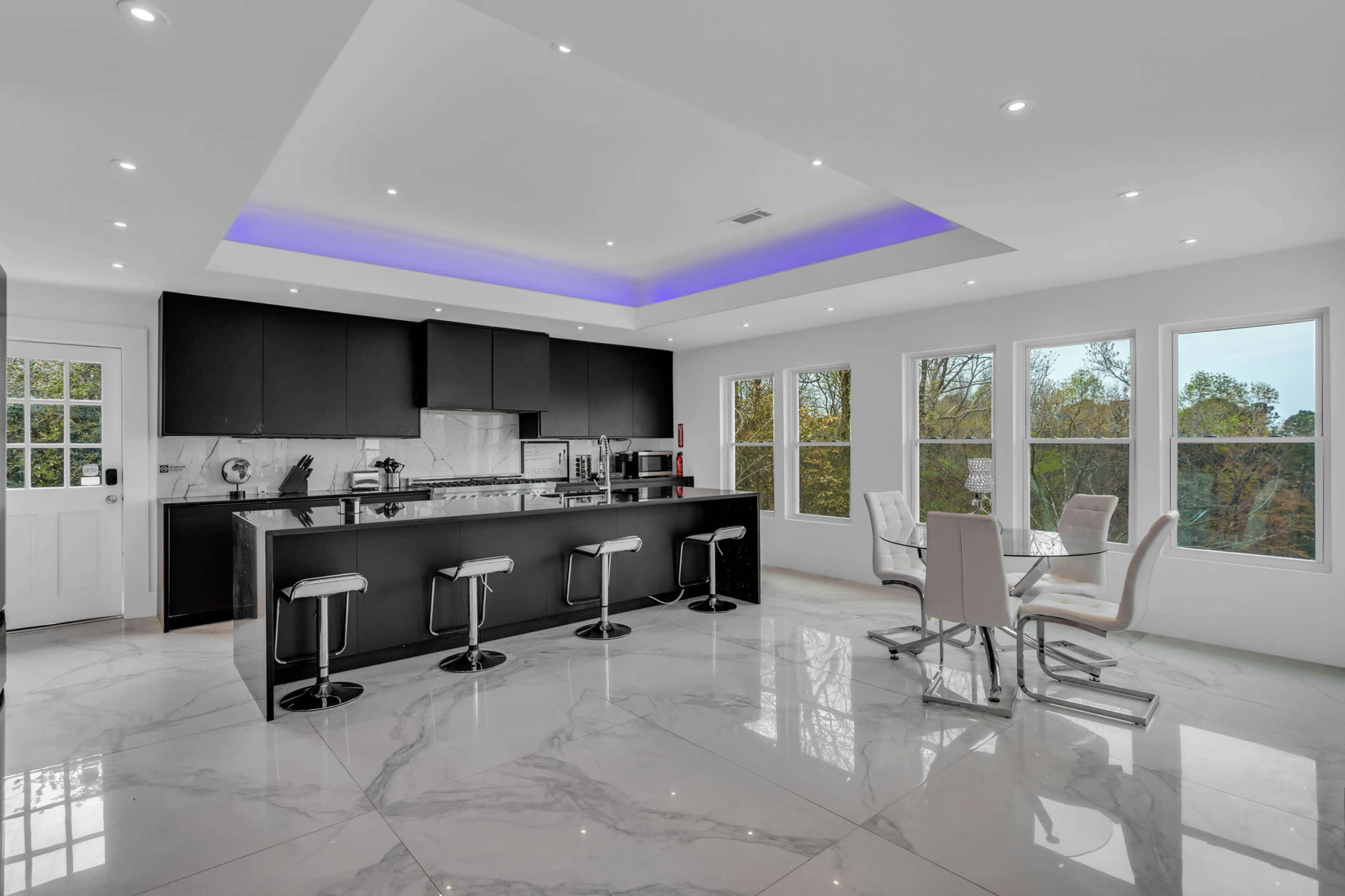 A modern kitchen featuring a large island with bar stools, sleek black cabinetry, and large windows letting in natural light.