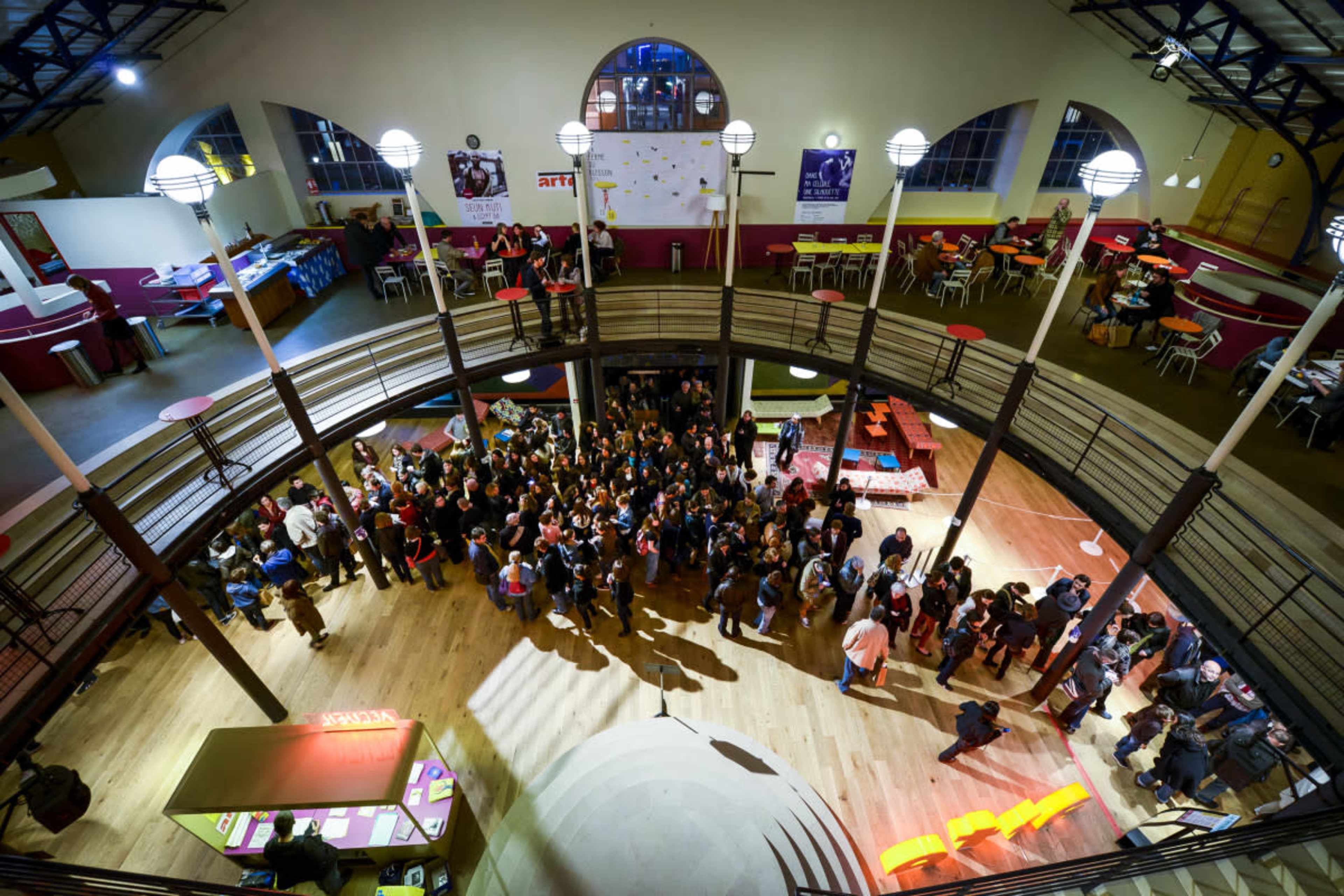 A large group of people gathers in the center of a spacious, modern venue with a circular design and multiple levels.