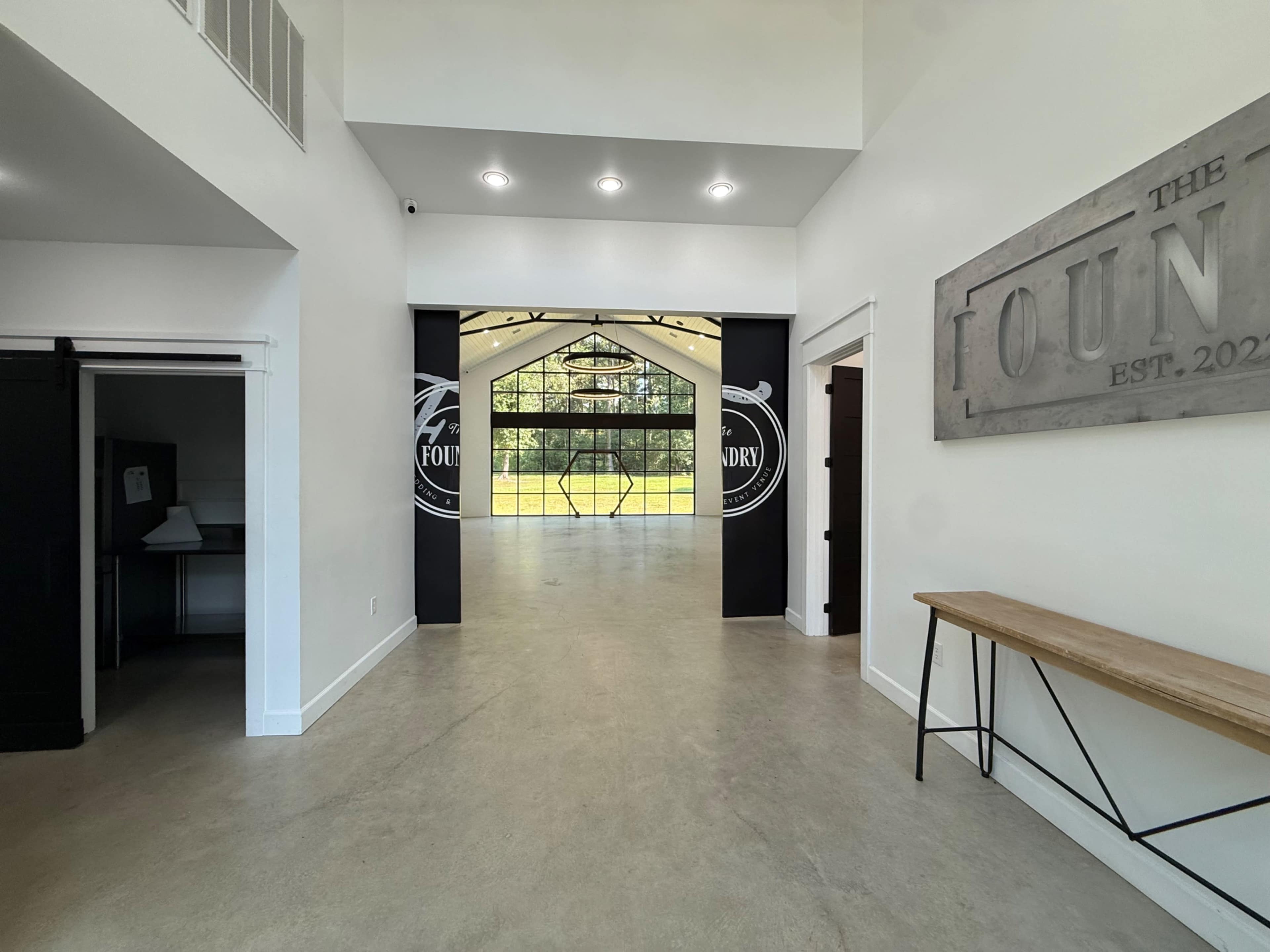 The image shows a spacious indoor entryway leading to a brightly-lit, modern event space with large windows overlooking a grassy area.