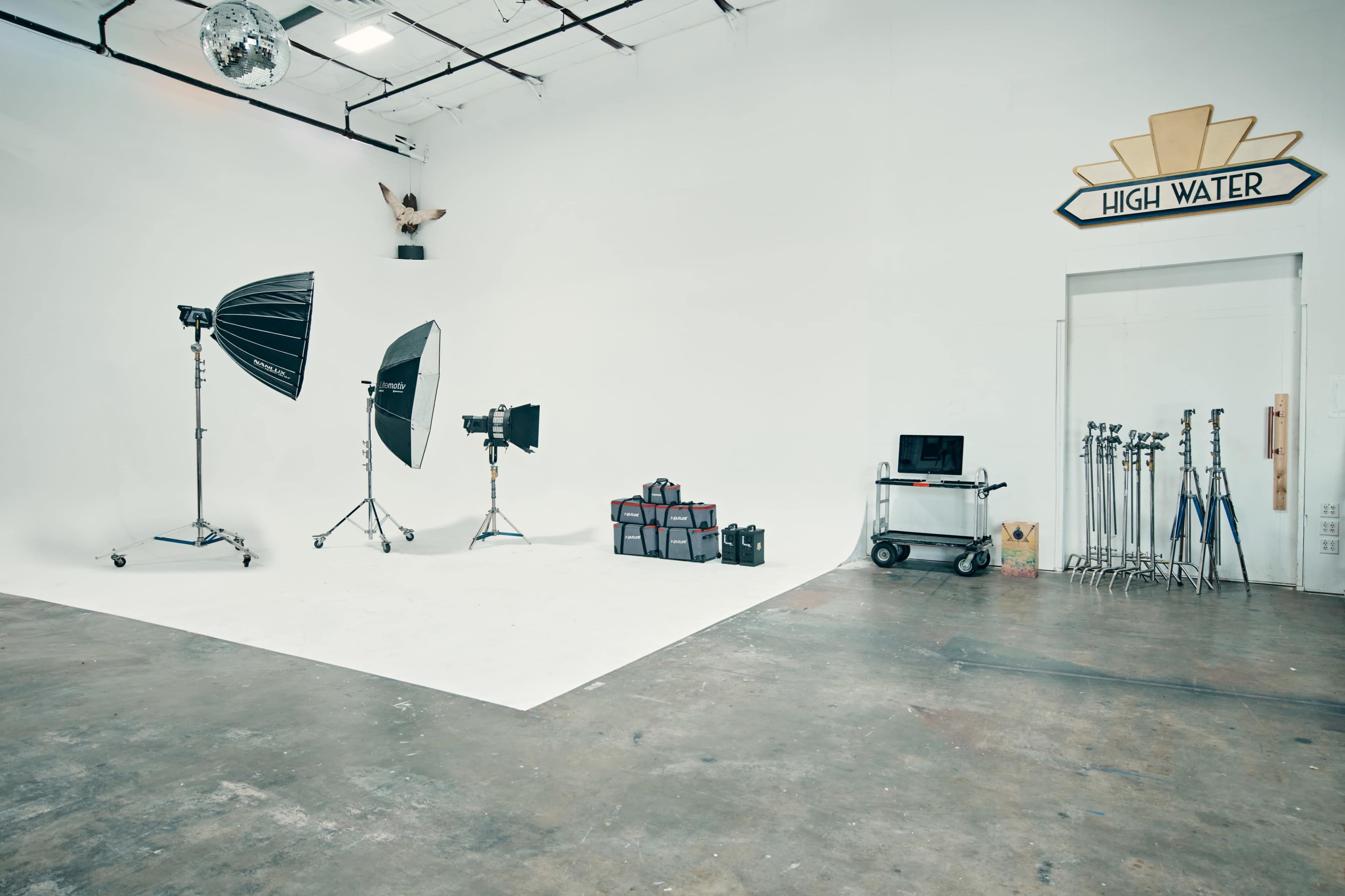 A photography studio with lighting equipment, a backdrop, and various tools arranged on the floor and against the wall.