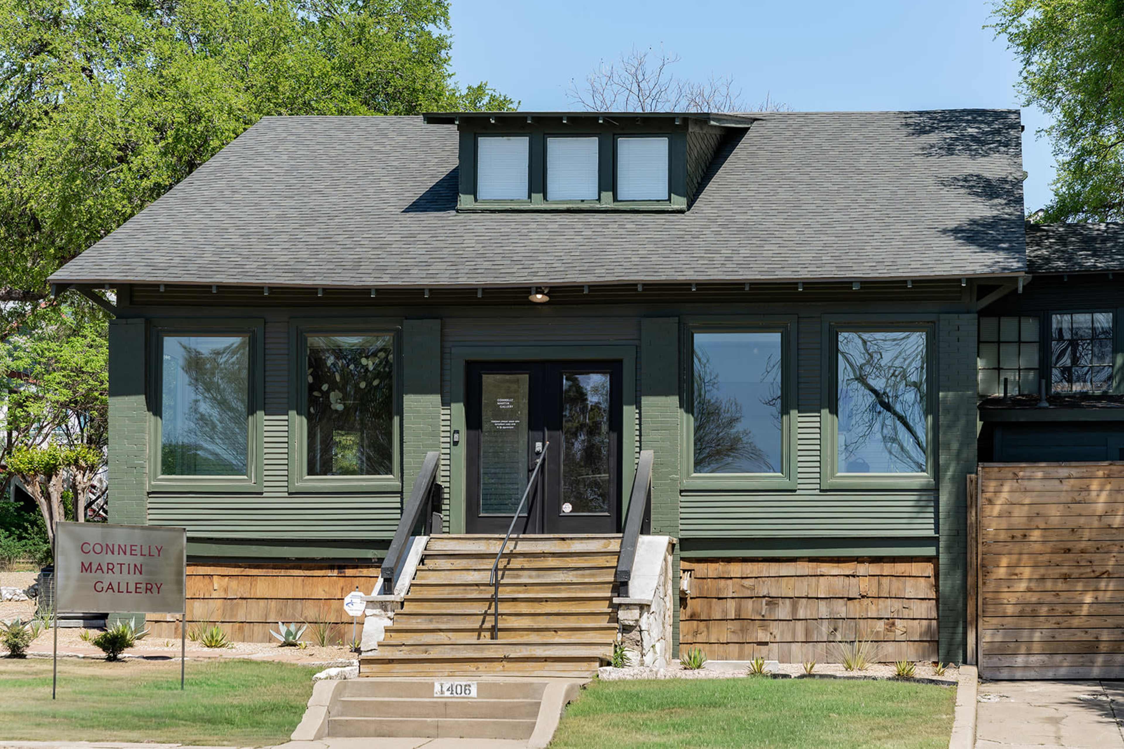 A green, two-story building with large front windows and a sign reading "Connelly Martin Gallery" is set on a landscaped lot.
