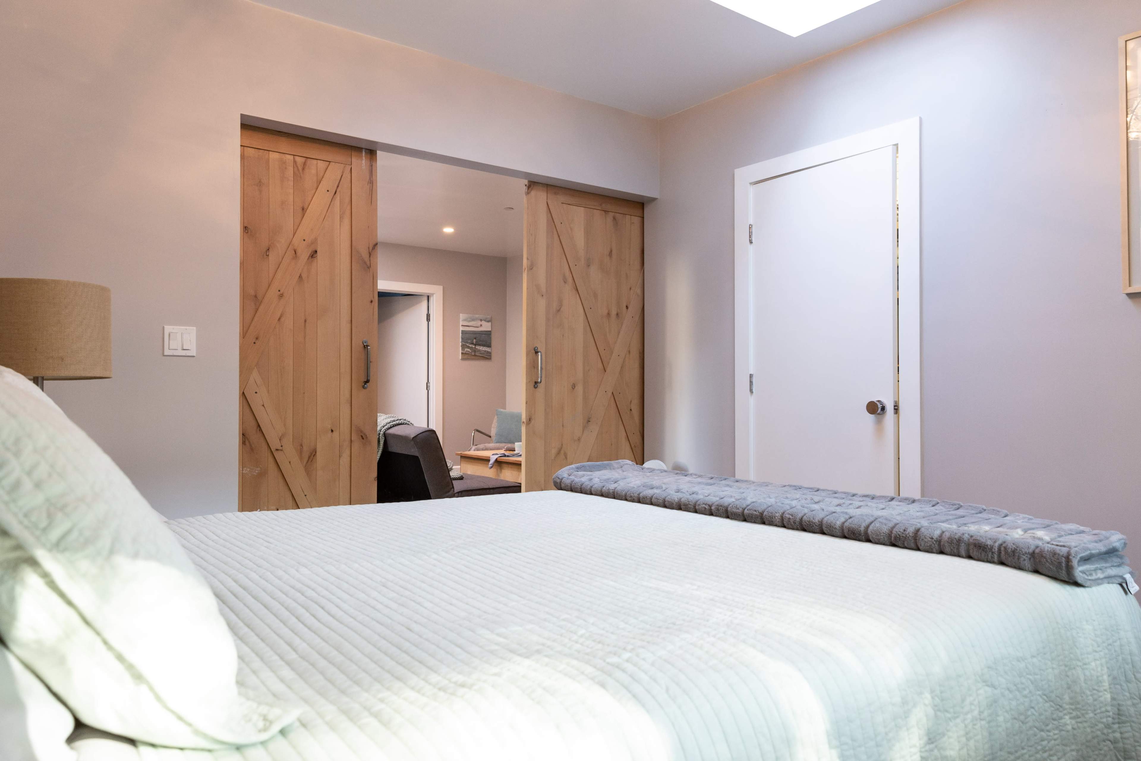 A softly lit bedroom with a bed in the foreground and wooden sliding doors leading to another room in the background.