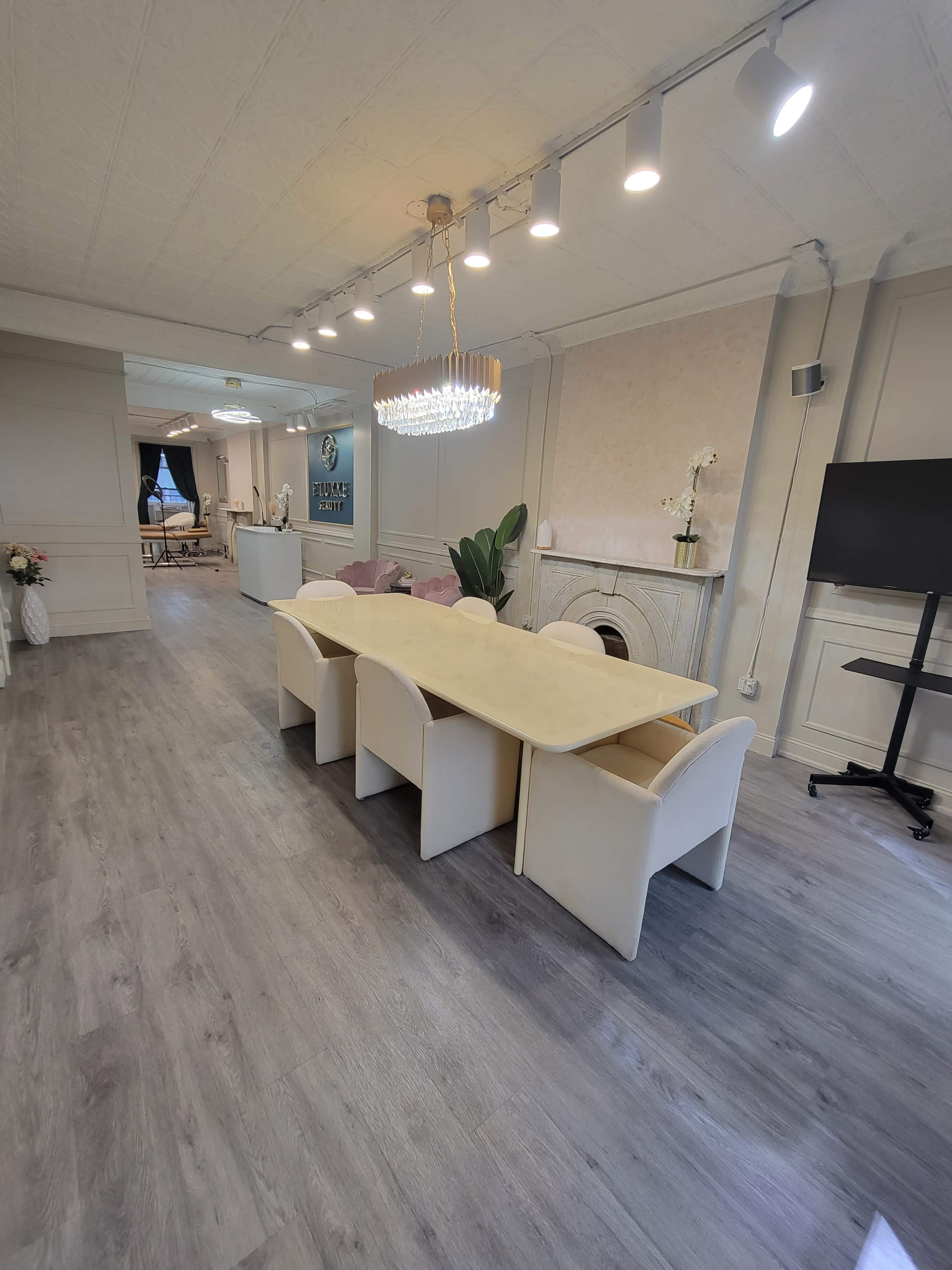 The image shows a modern meeting room with a long table surrounded by white chairs, a chandelier overhead, and a television mounted on the wall.