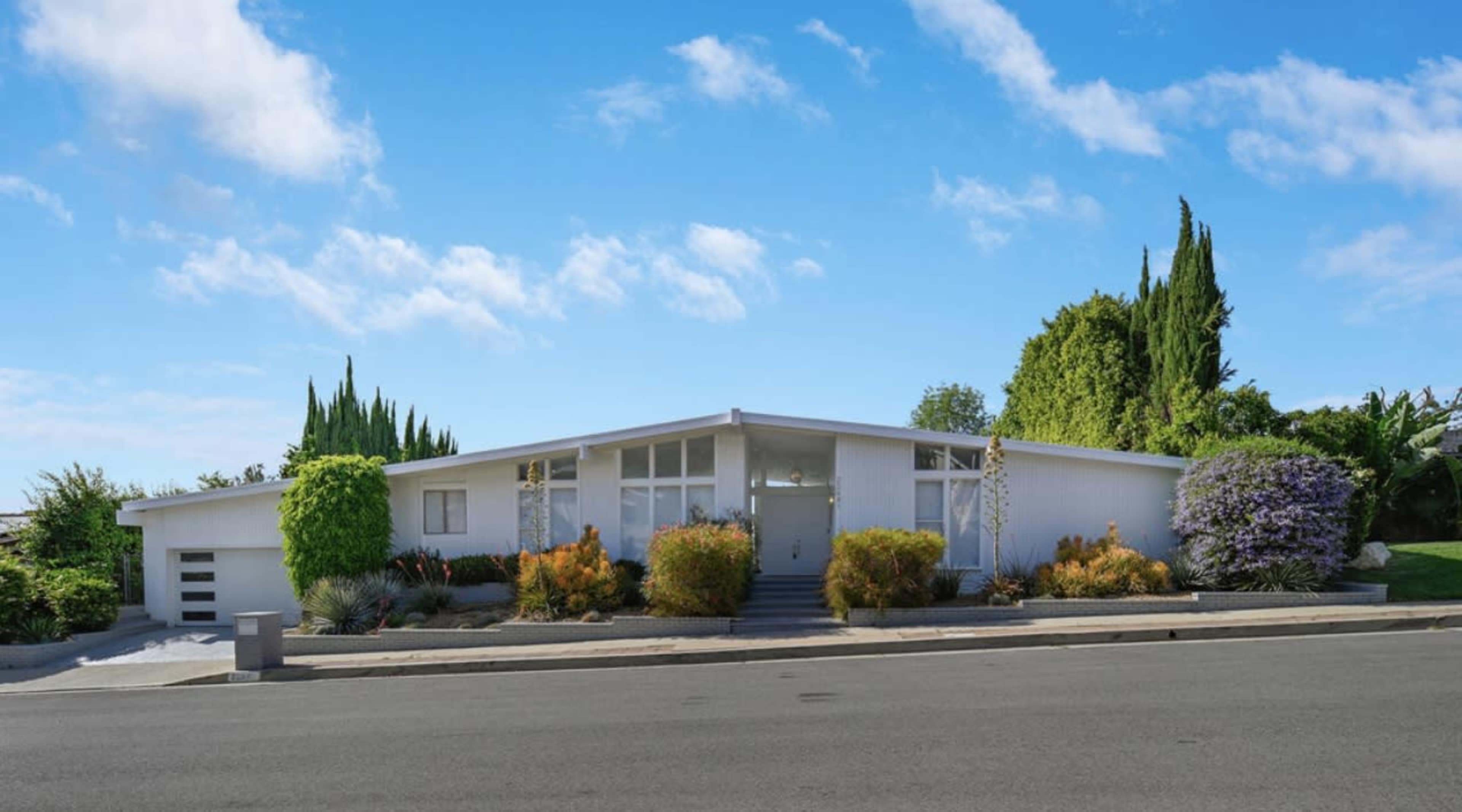 A modern white house with a landscaped front yard and a clear blue sky.