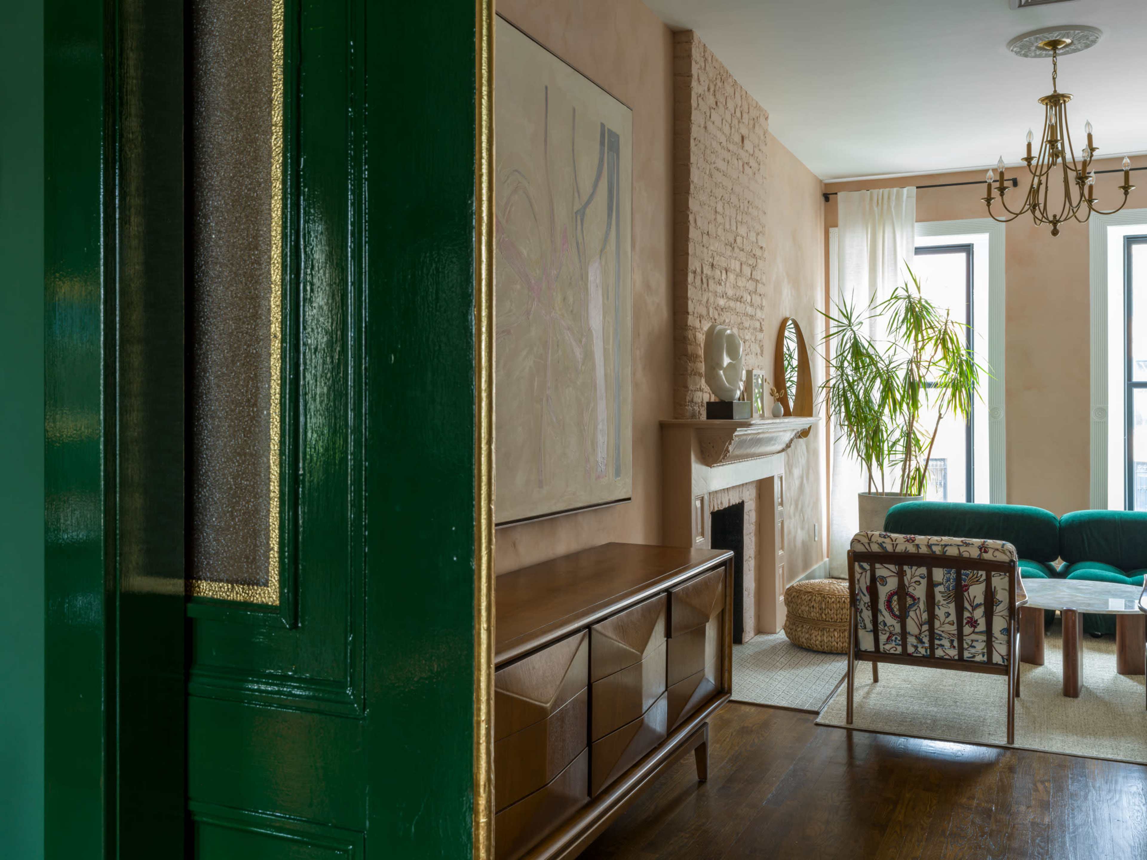 A green door opens to reveal a living room featuring a fireplace, a teal sofa, and large windows with sheer curtains.