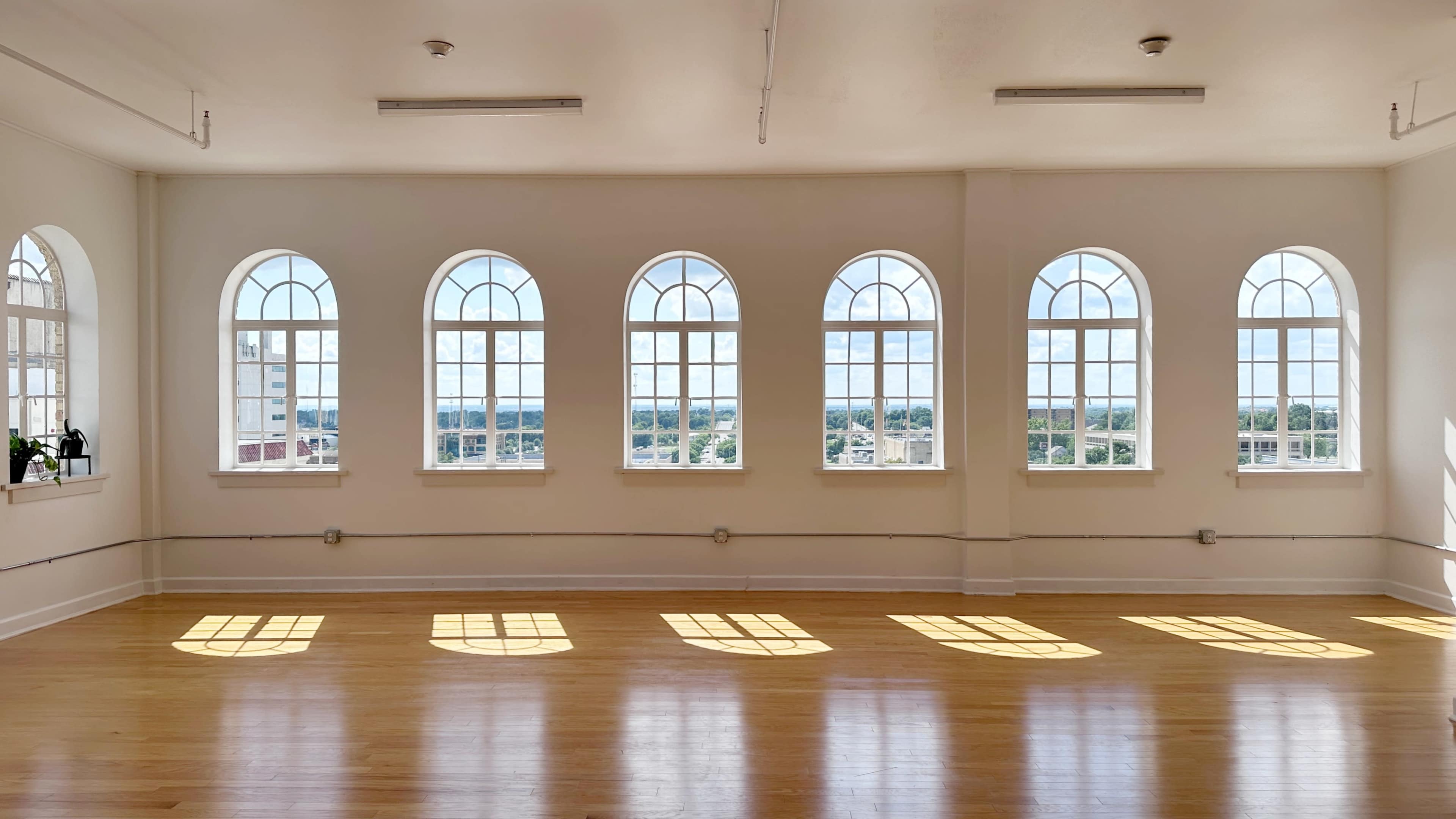 The image shows a bright, spacious room with multiple arched windows casting shadows on the polished wooden floor.