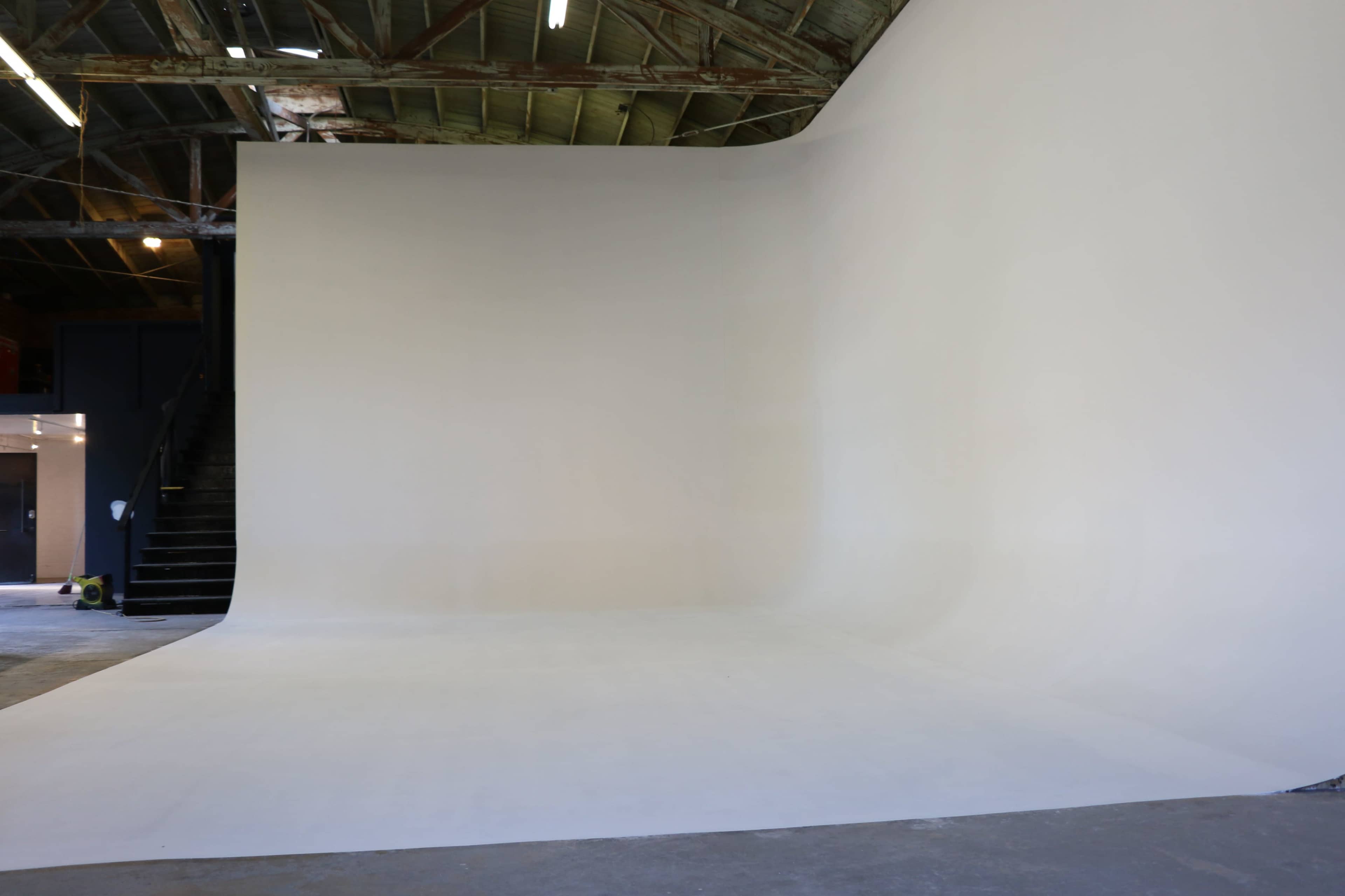The image shows a large, minimalist photography studio with a seamless white backdrop and an open, industrial-style space.