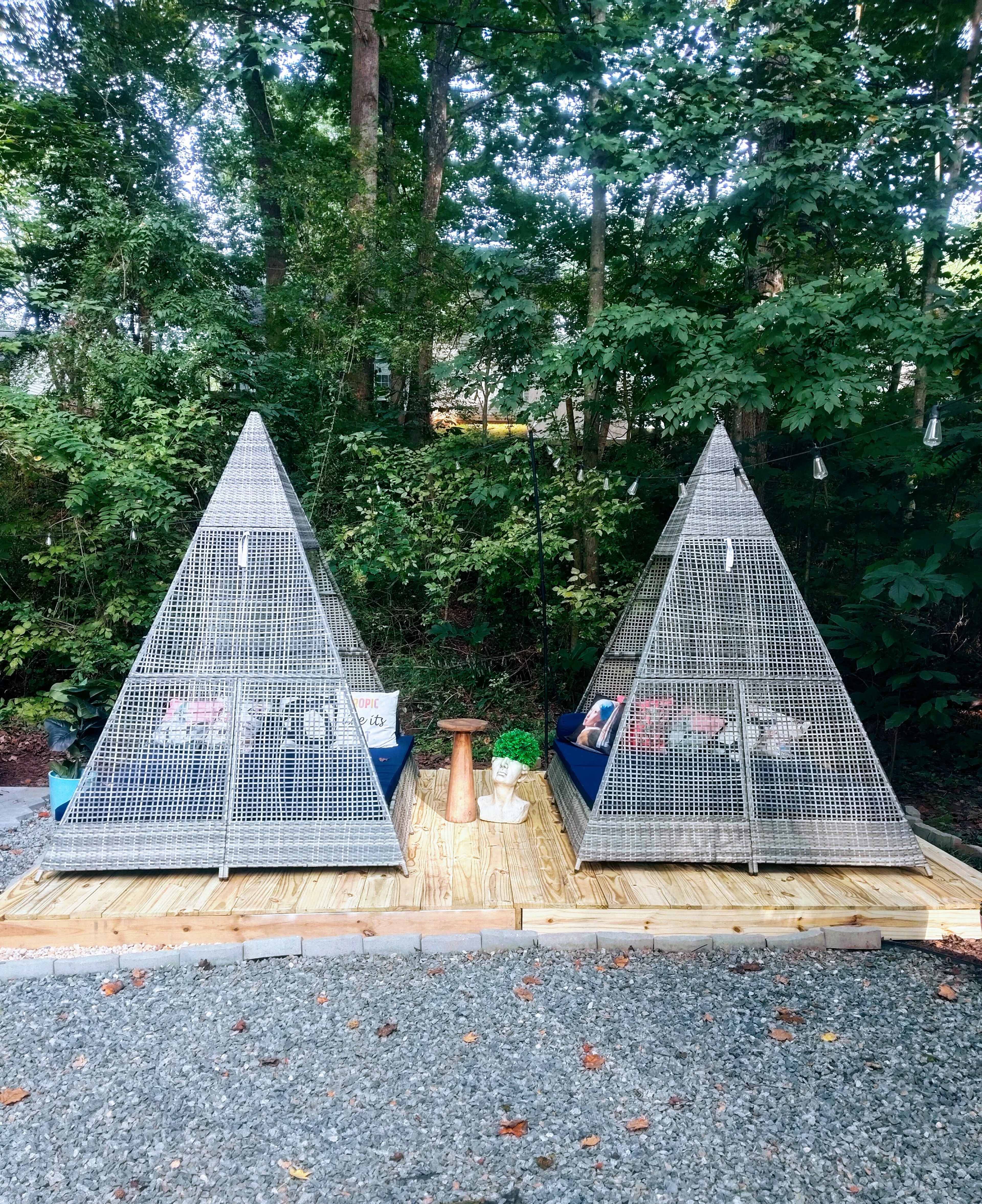 The image shows two triangular metal structures with open sides, placed on a wooden deck surrounded by trees.