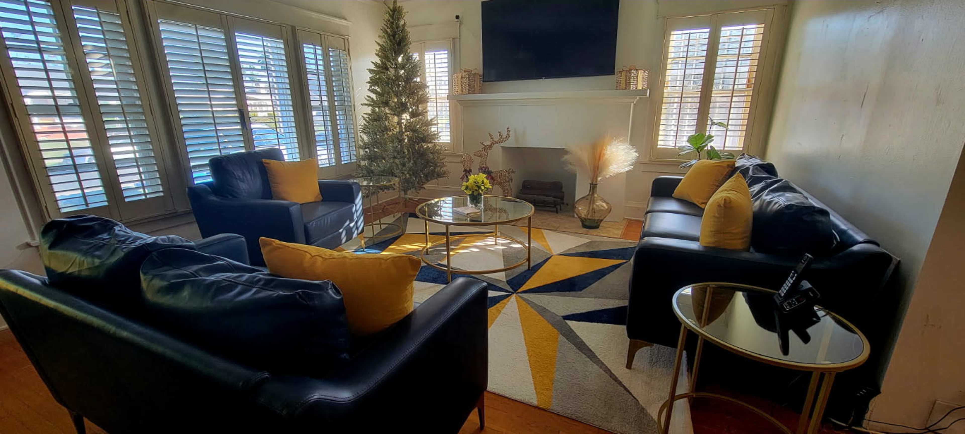A living room features black leather sofas with yellow cushions, a glass coffee table, and a decorated corner with a Christmas tree.