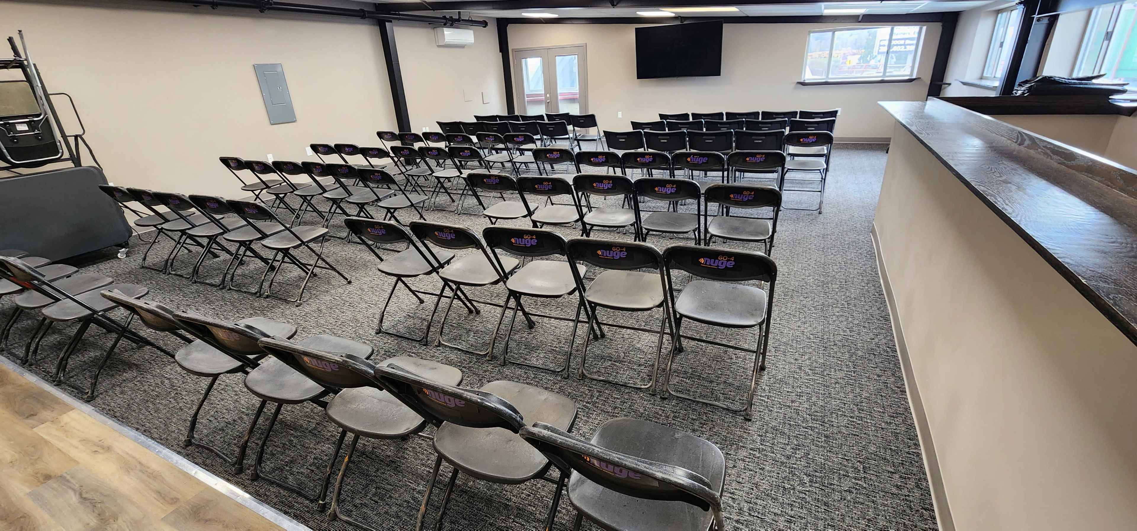 A room with neatly arranged folding chairs facing a blank wall, with a small stage area at one end.