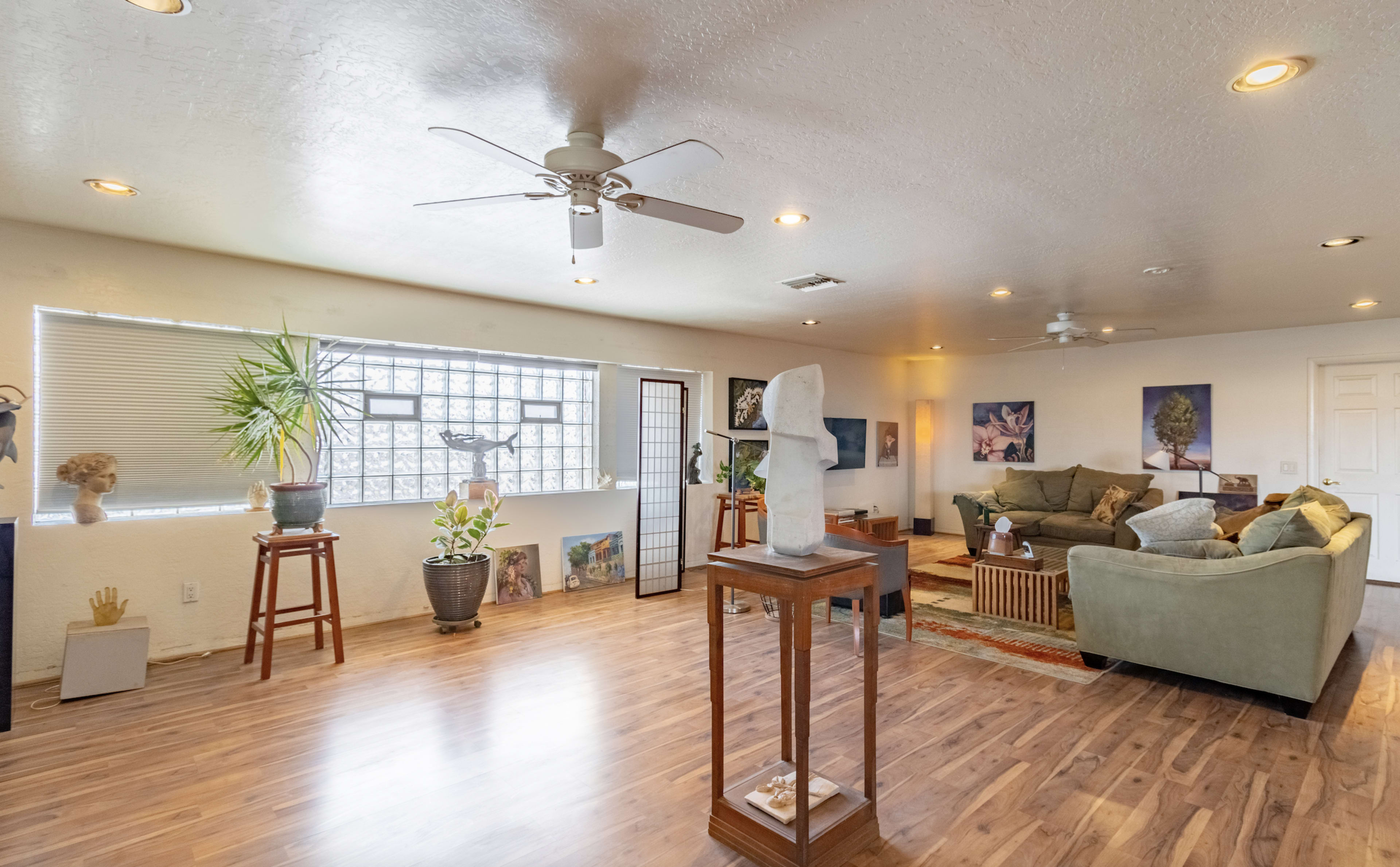 A spacious living room with hardwood floors, a green sofa, decorative plants, and a sculpture on a pedestal.