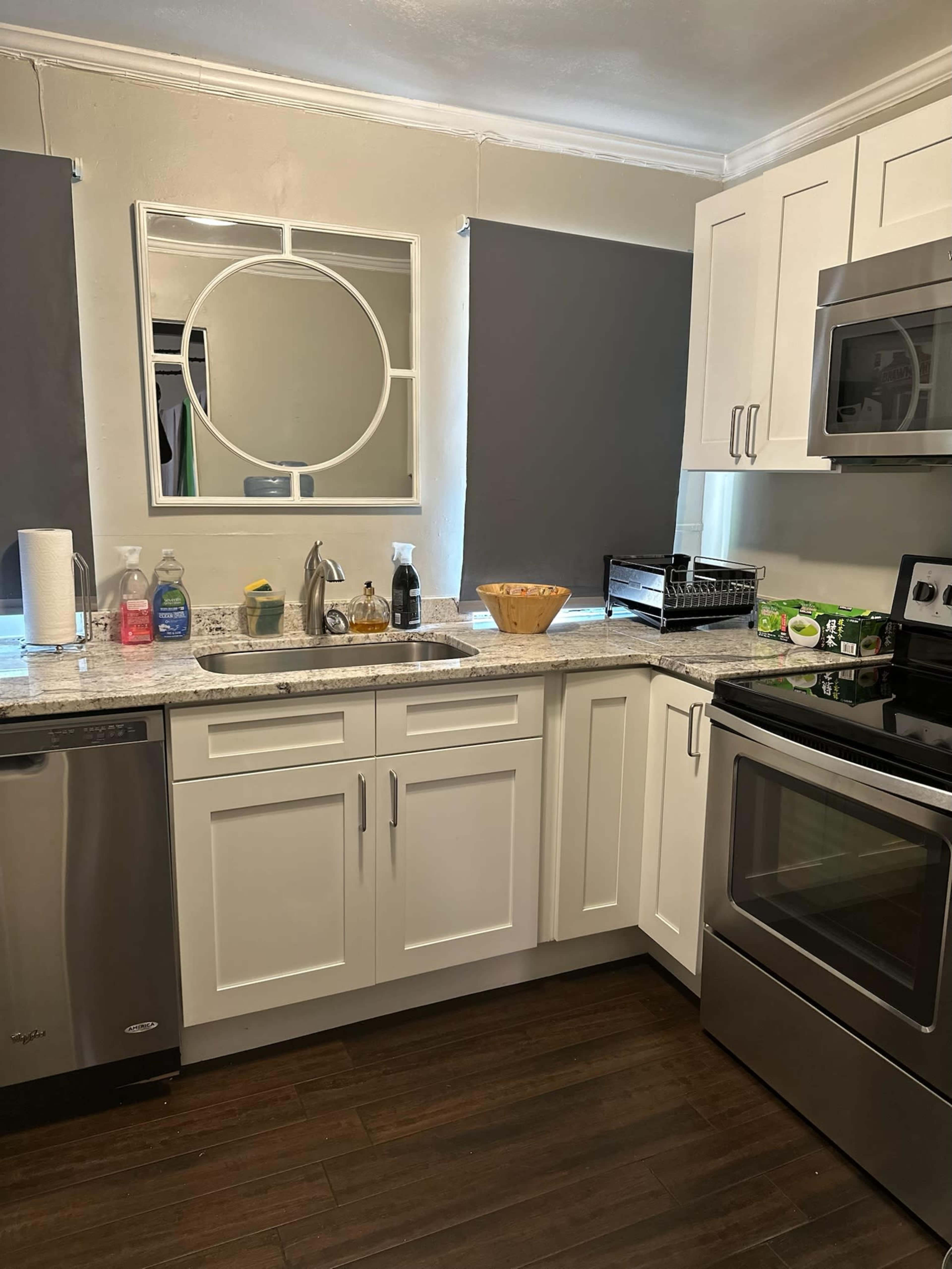 A modern kitchen with white cabinets, a stainless steel dishwasher, and a round mirror above the sink.