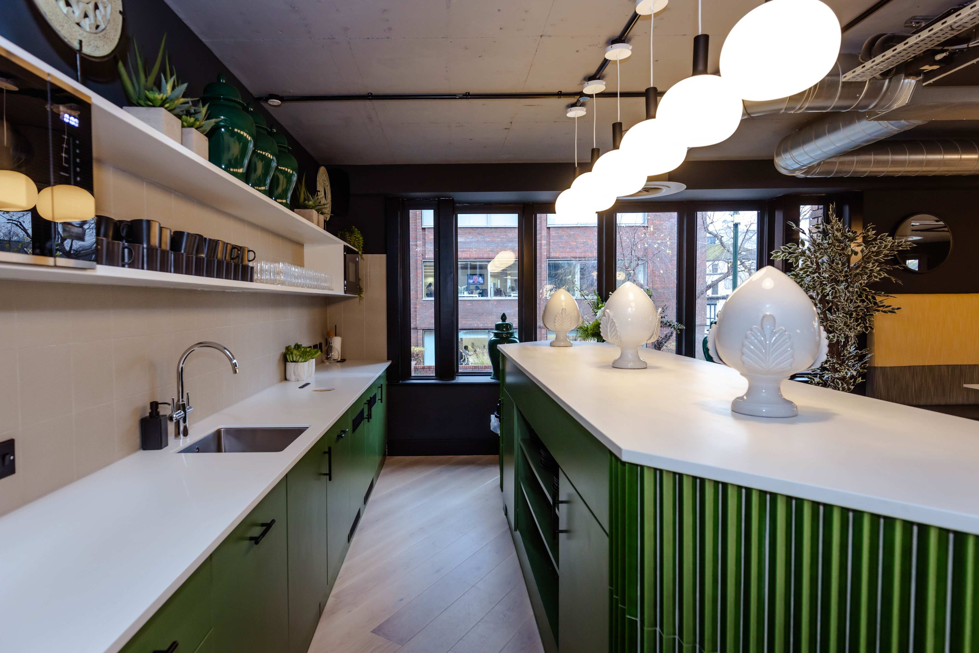 A modern kitchen features green cabinetry, a long white countertop, and a series of round light fixtures above.
