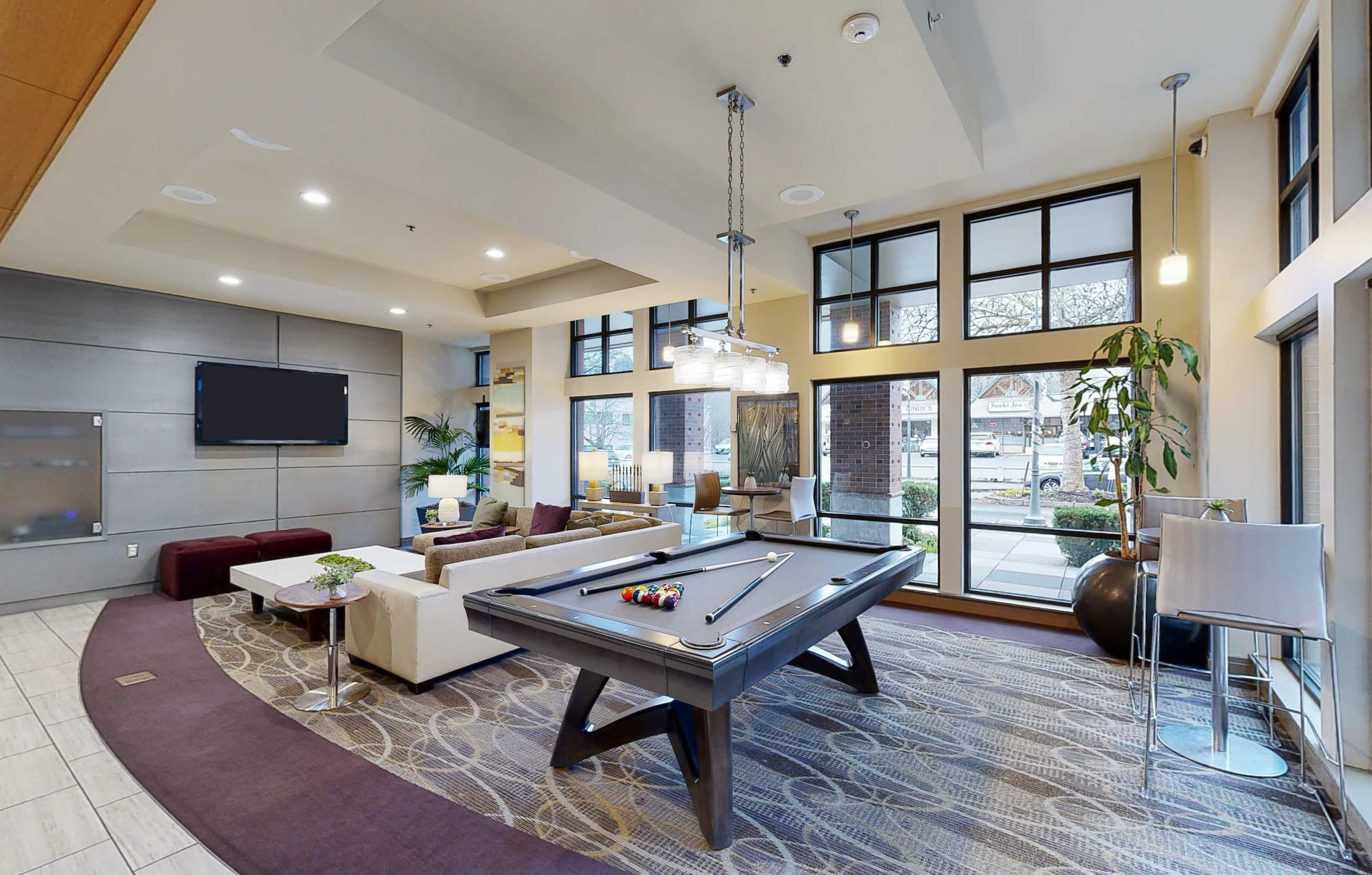 A modern lounge space featuring a pool table, comfortable seating, large windows, and a flat-screen television.