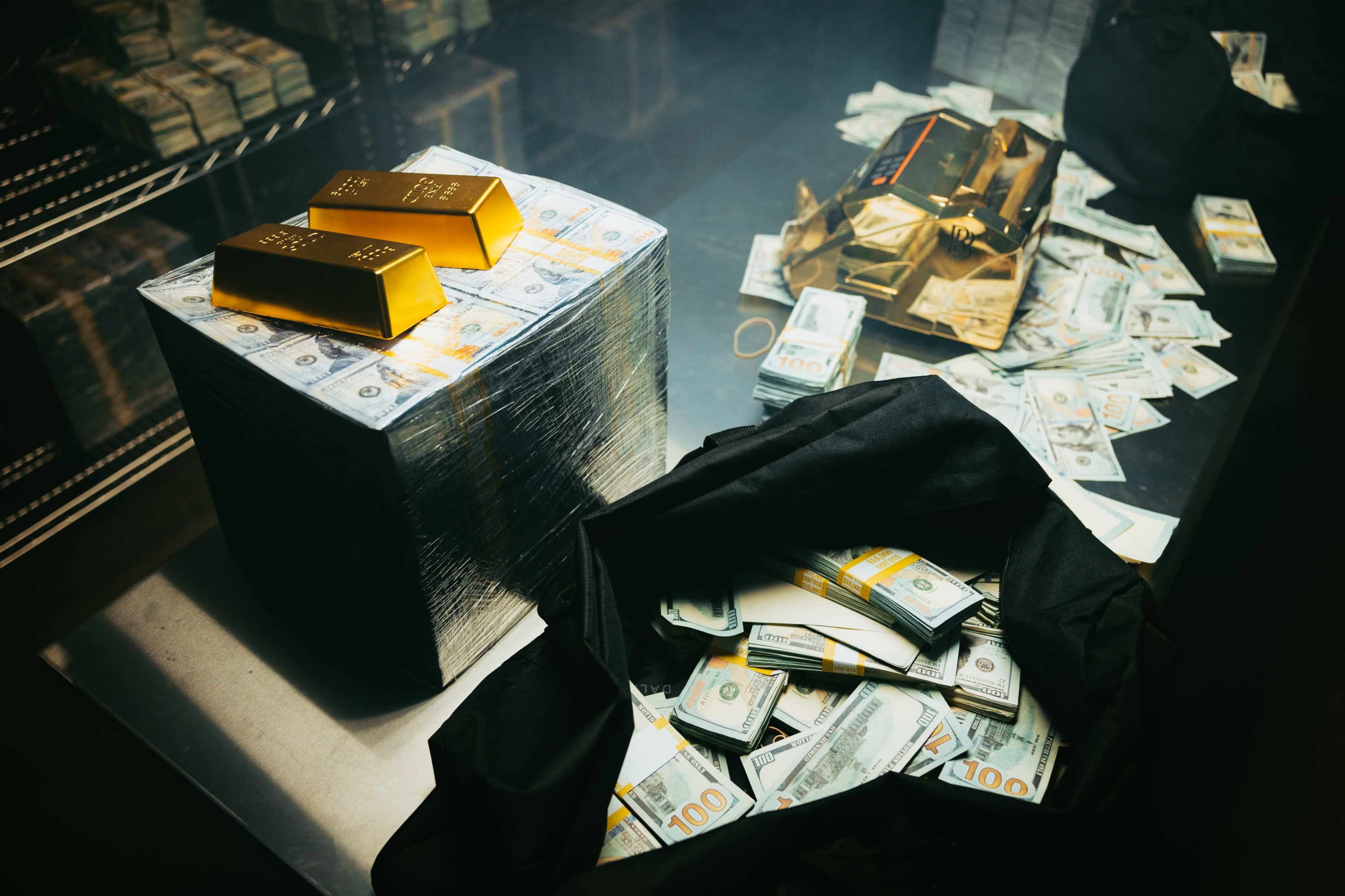 The image shows a stack of cash wrapped in plastic next to two gold bars, with more scattered cash around a black bag on a metallic table.