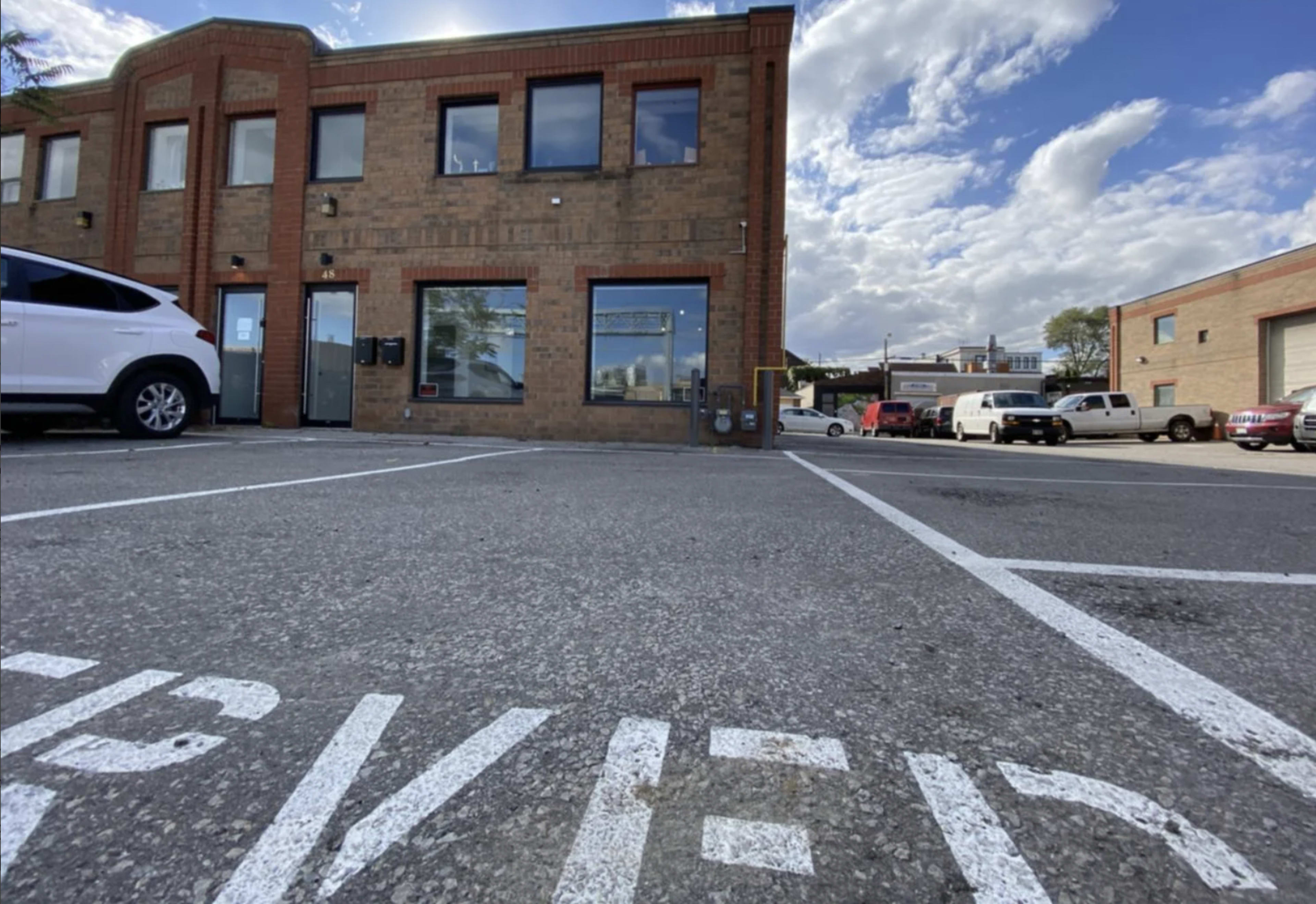 A parking lot in front of a brick building with multiple windows under a partly cloudy sky.