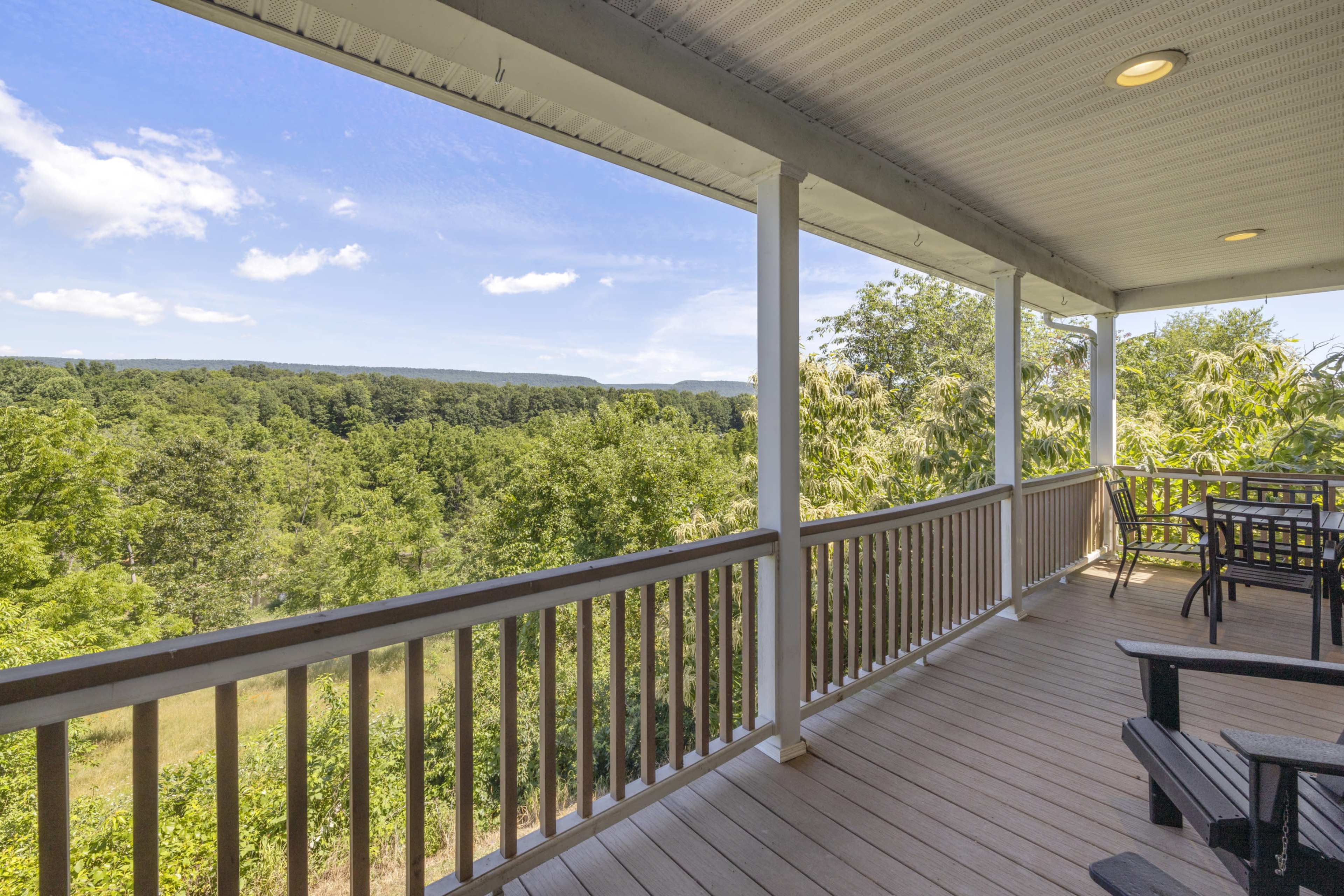 A spacious porch overlooks a scenic landscape of trees and rolling hills under a clear blue sky.