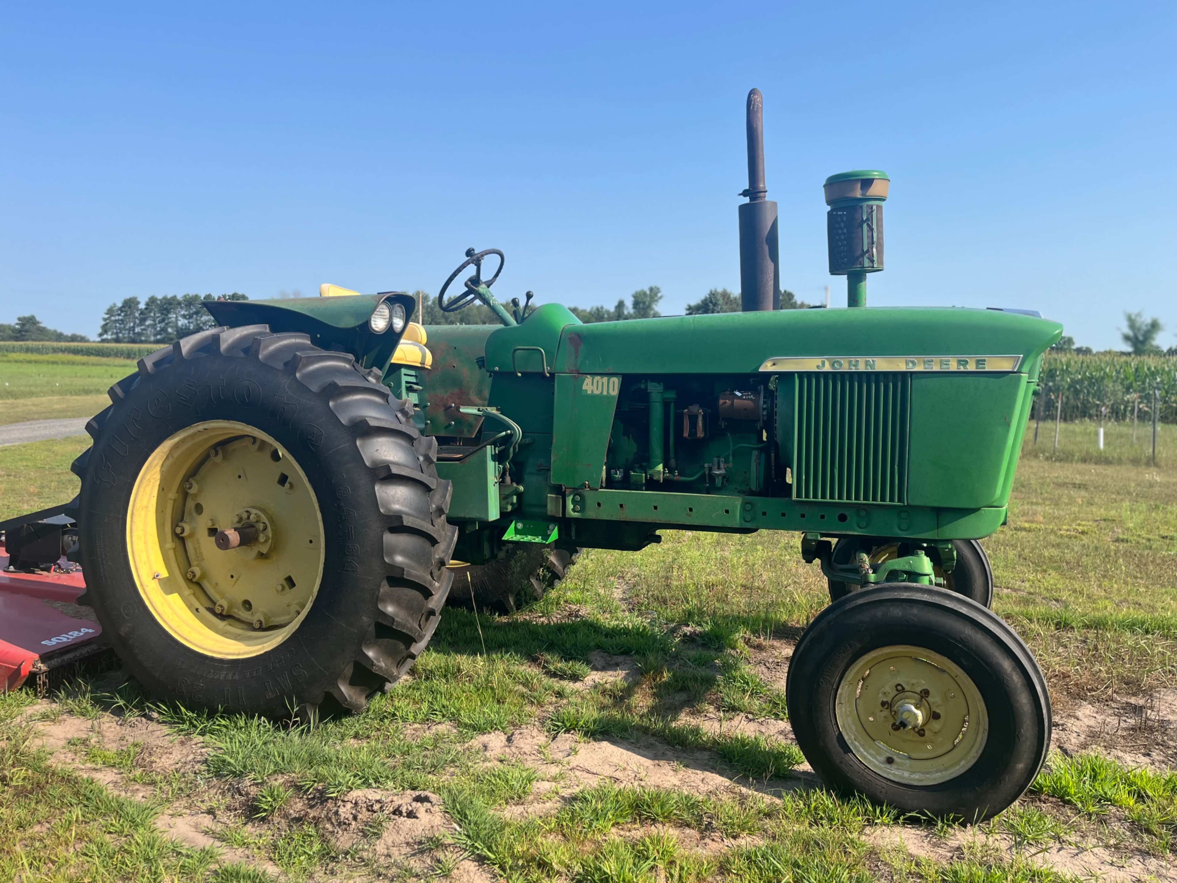 A green John Deere 4010 tractor is parked on a grassy field with trees in the background.