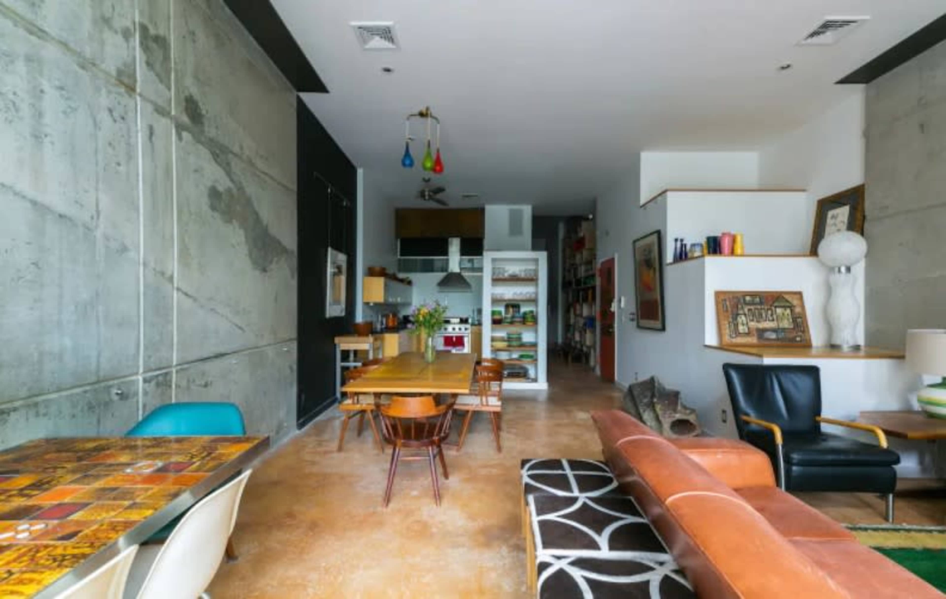 A modern, minimalist open-concept living space with concrete walls, a dining area with a wooden table, and a seating area featuring a leather sofa.