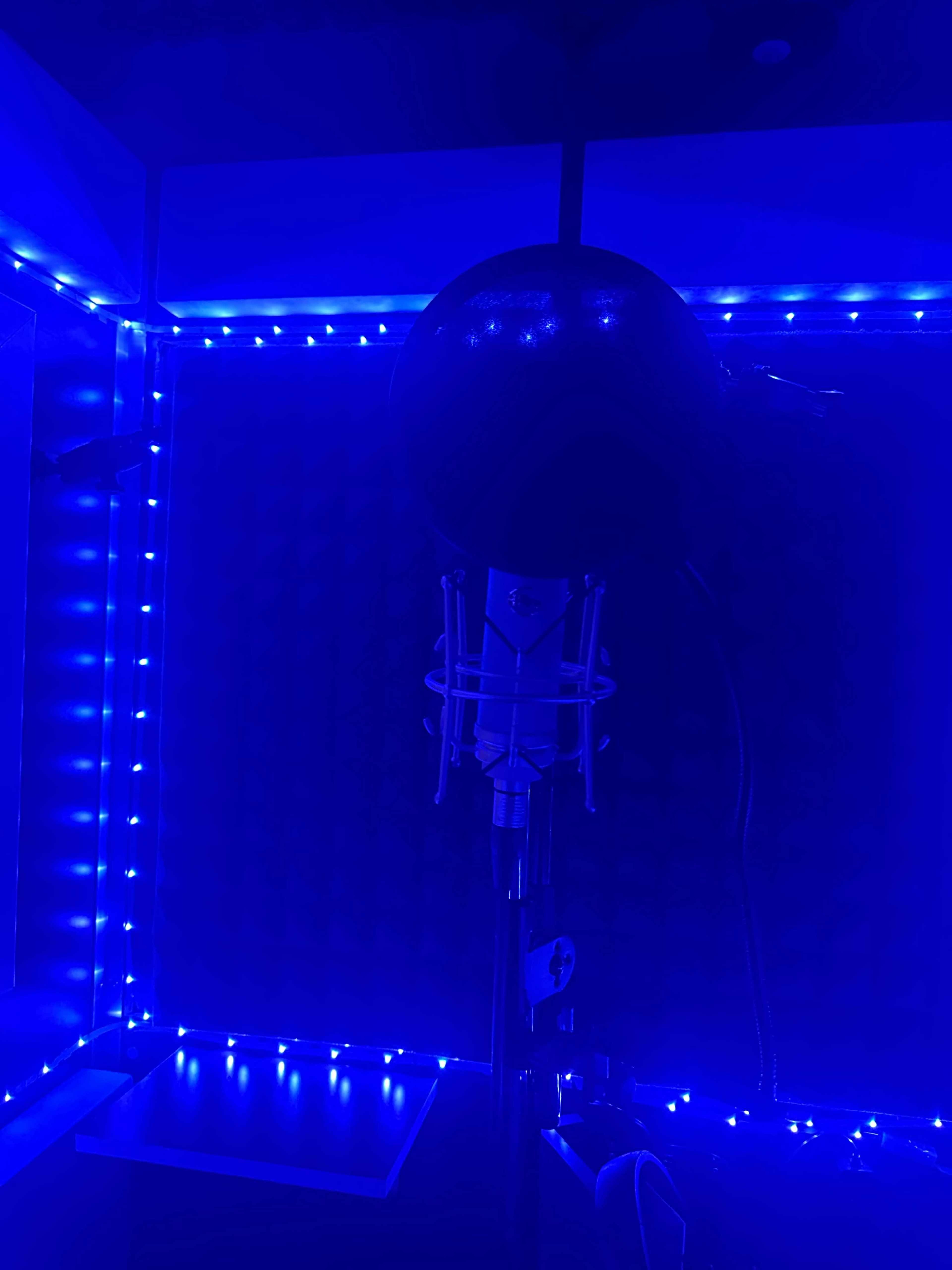 A microphone stands in a blue-lit recording booth surrounded by illuminated decor.