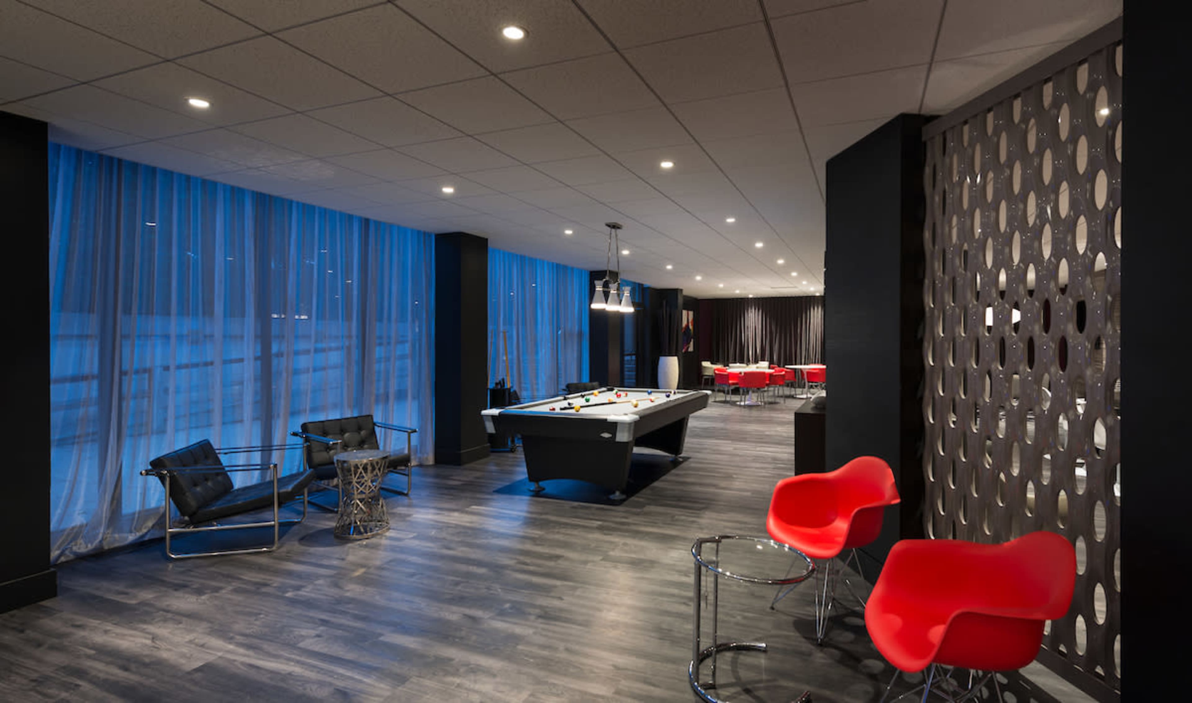 A modern lounge area with a pool table, stylish seating, and large windows draped with sheer curtains.