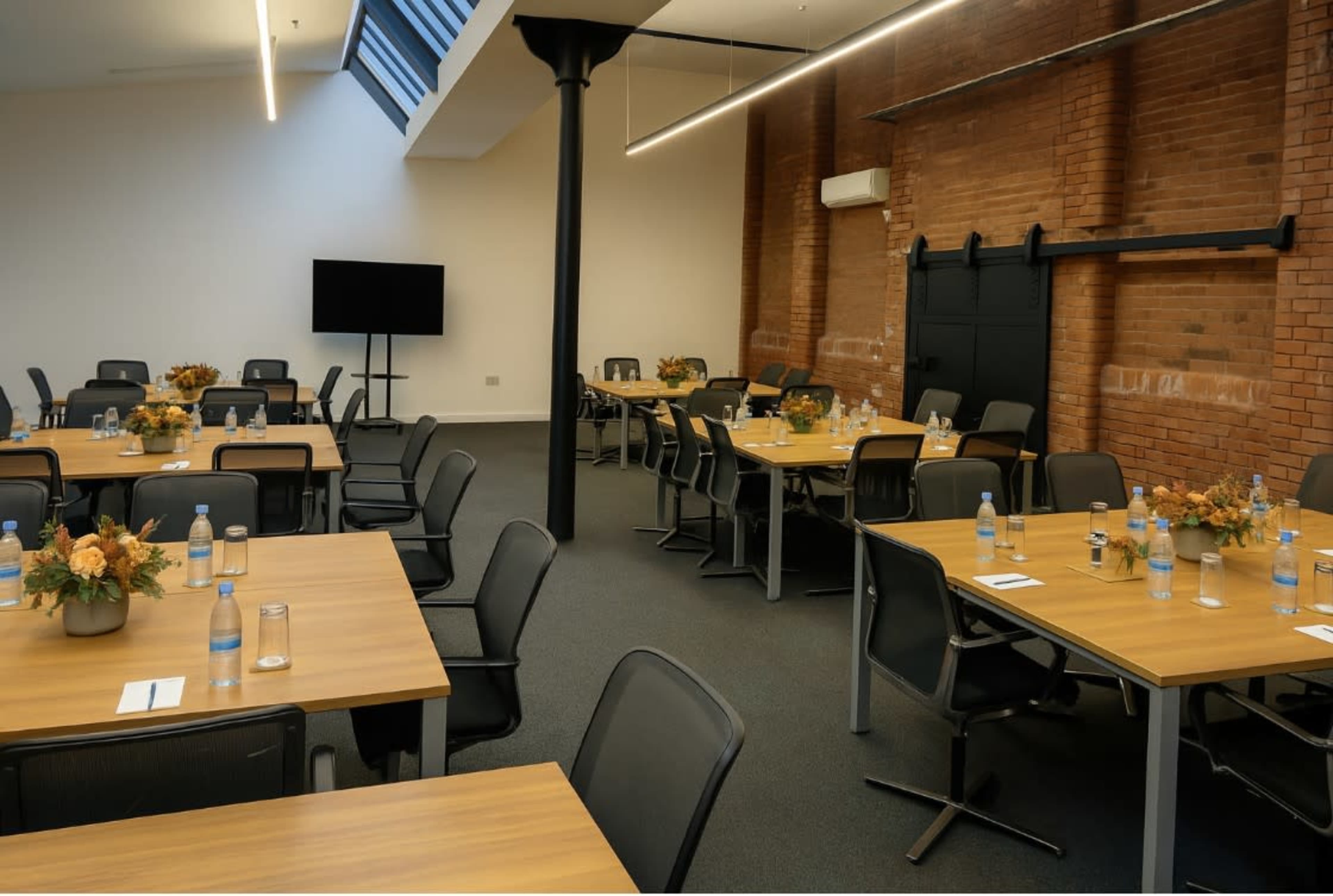 A modern meeting room features several tables arranged for discussions, with water bottles and floral centerpieces on each table.