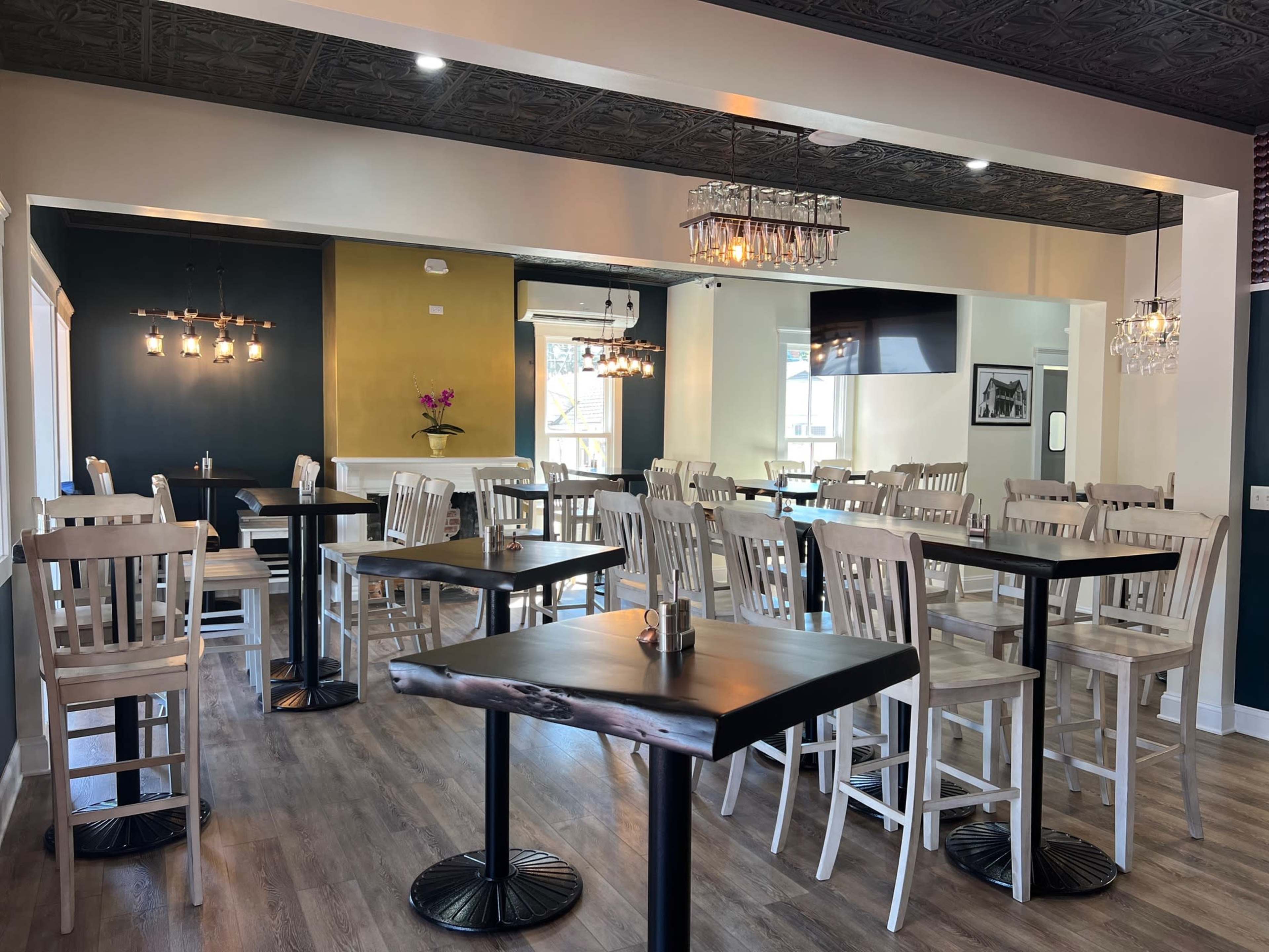 A modern restaurant interior with rows of simple white wooden tables and chairs arranged neatly on a wooden floor.