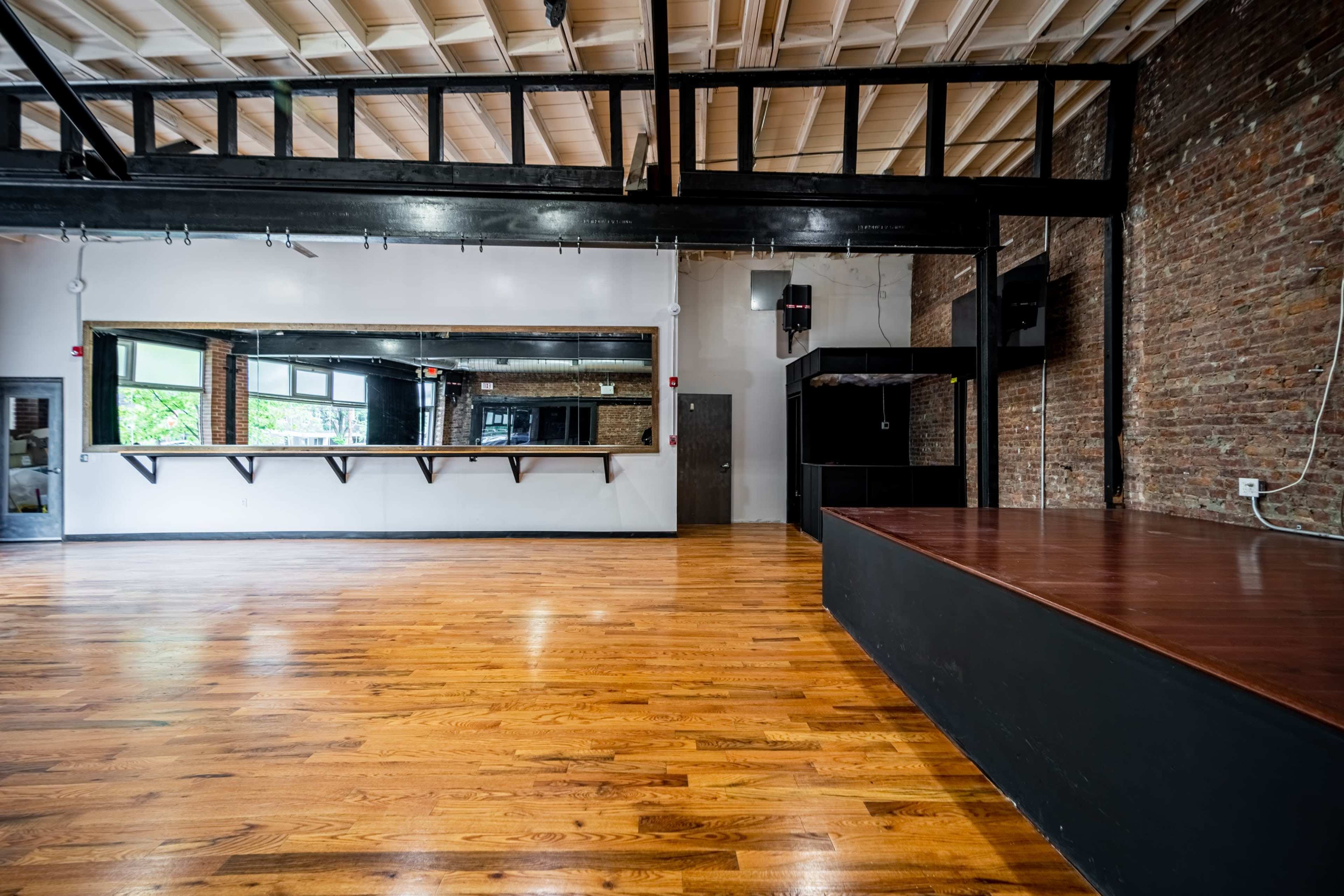 An empty wooden dance studio with exposed brick walls and large mirrors.