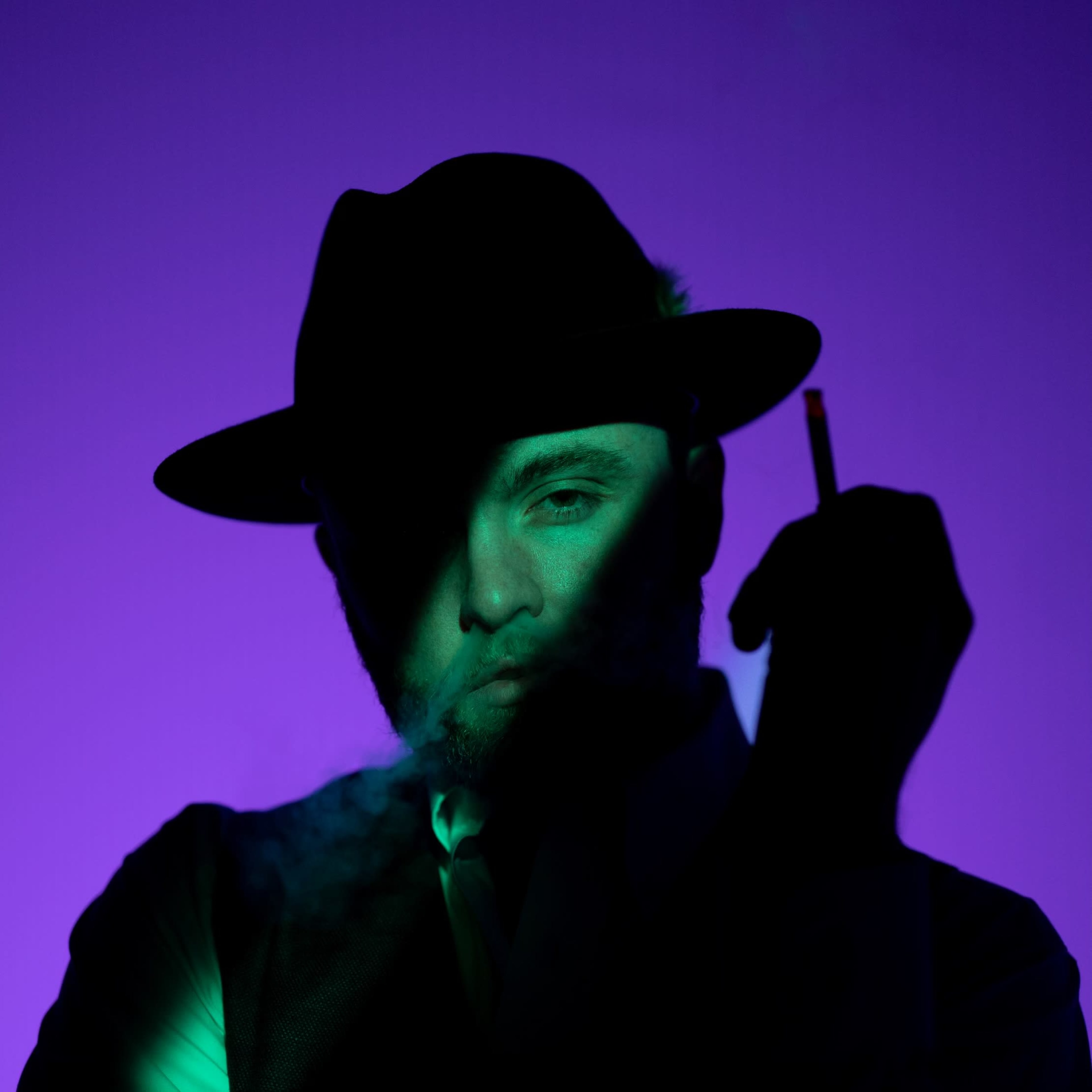 A man in a black hat holds a cigarette while partially obscured in shadow against a purple background.