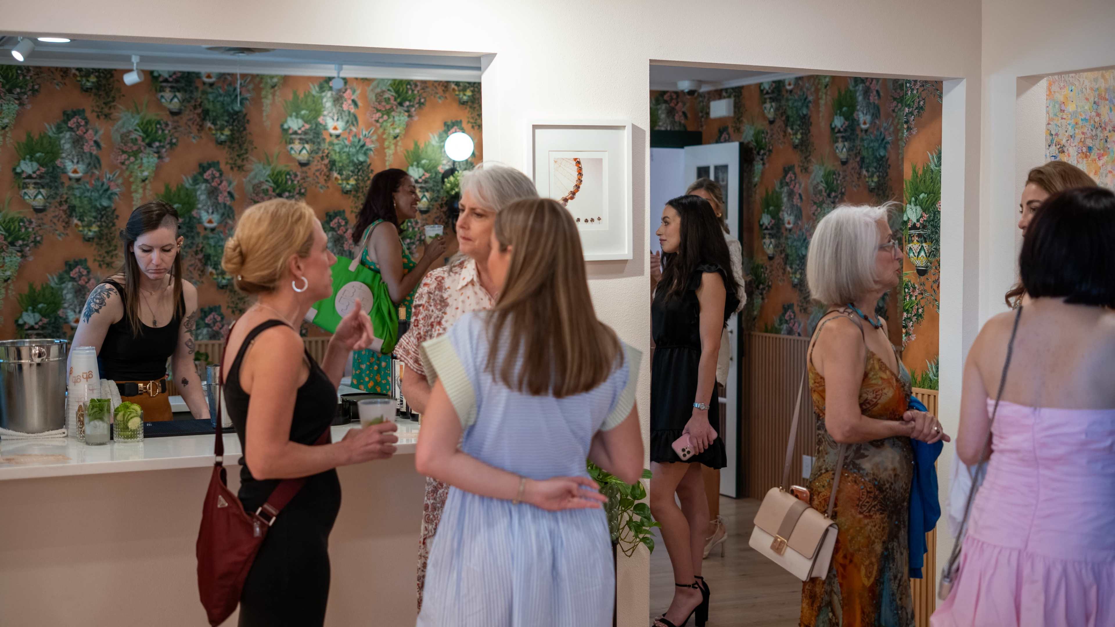 A group of people interacts in a brightly decorated interior, featuring floral wallpaper and a bar area.