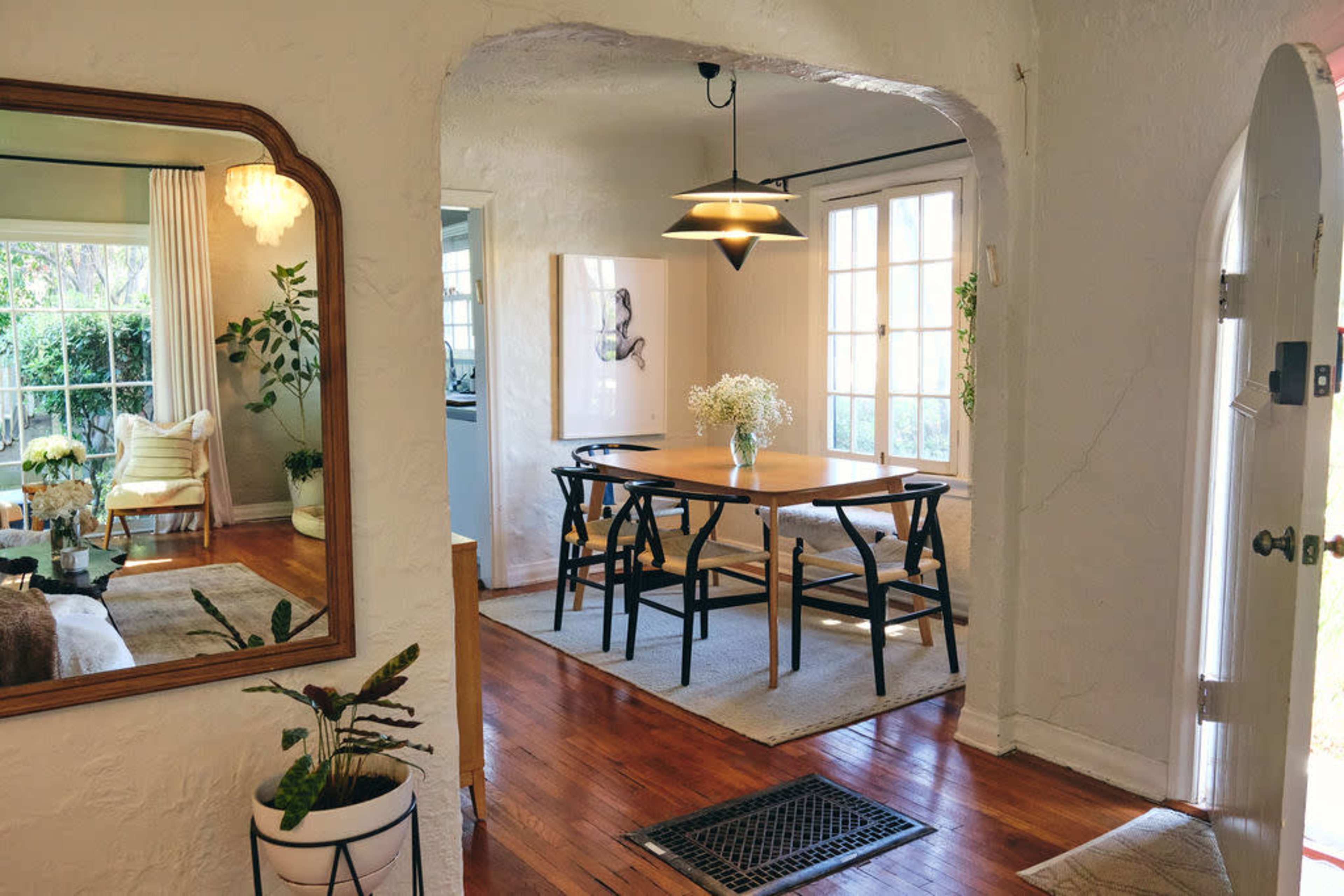 A dining area with a wooden table surrounded by black chairs is visible through an archway, with a view of a well-lit living room and indoor plants.