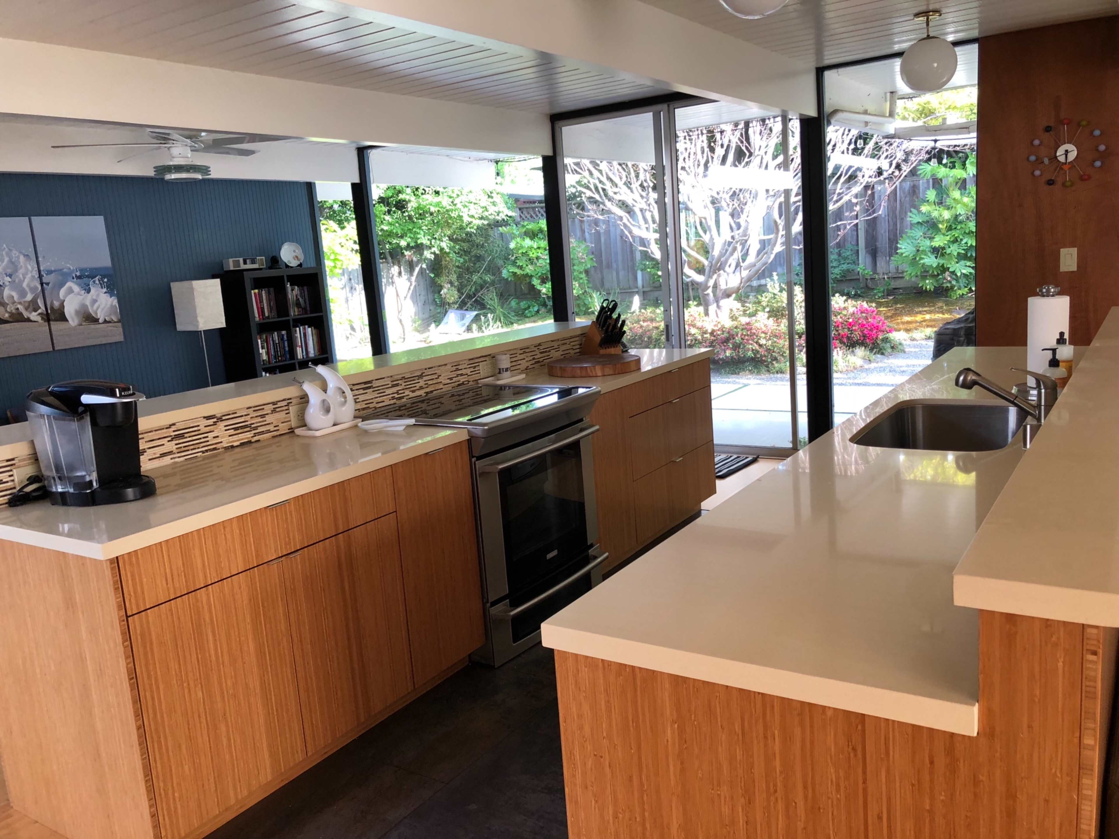 A modern kitchen with wooden cabinetry, a stainless steel oven, and large glass windows overlooking a landscaped garden.