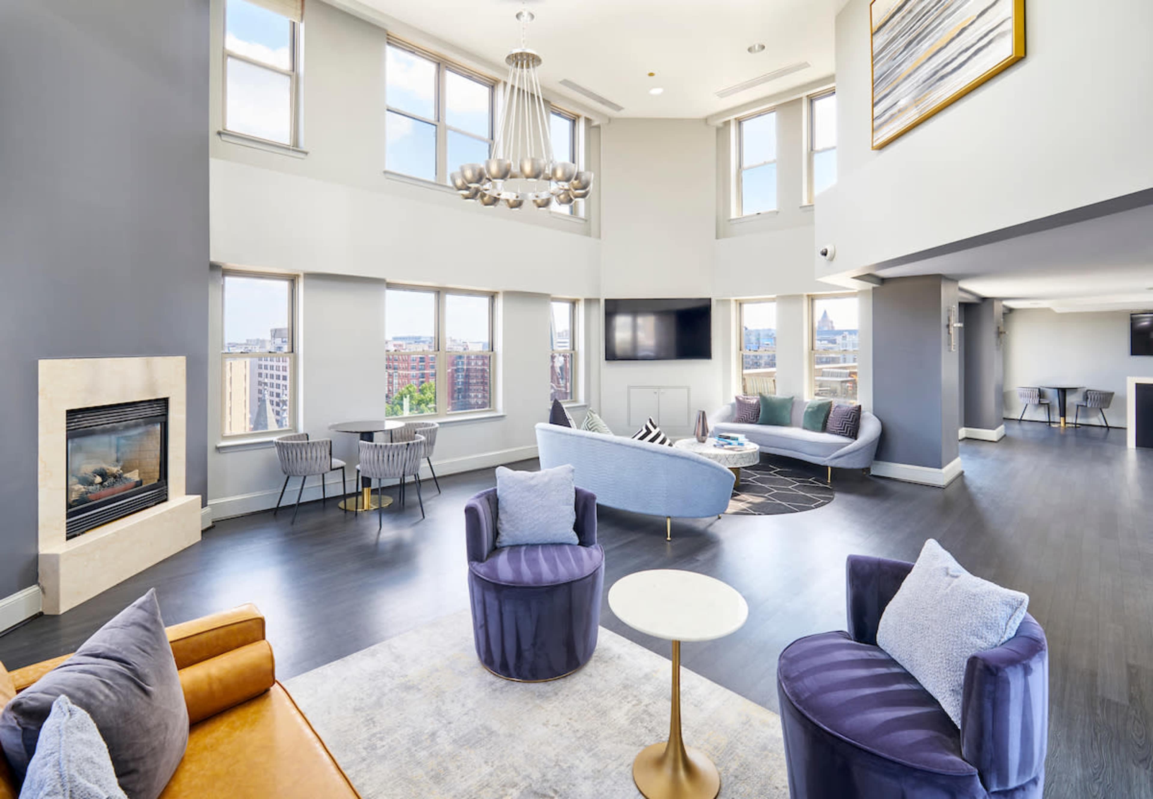 The image shows a spacious, modern living area with large windows, a fireplace, and contemporary furniture arranged for comfort.