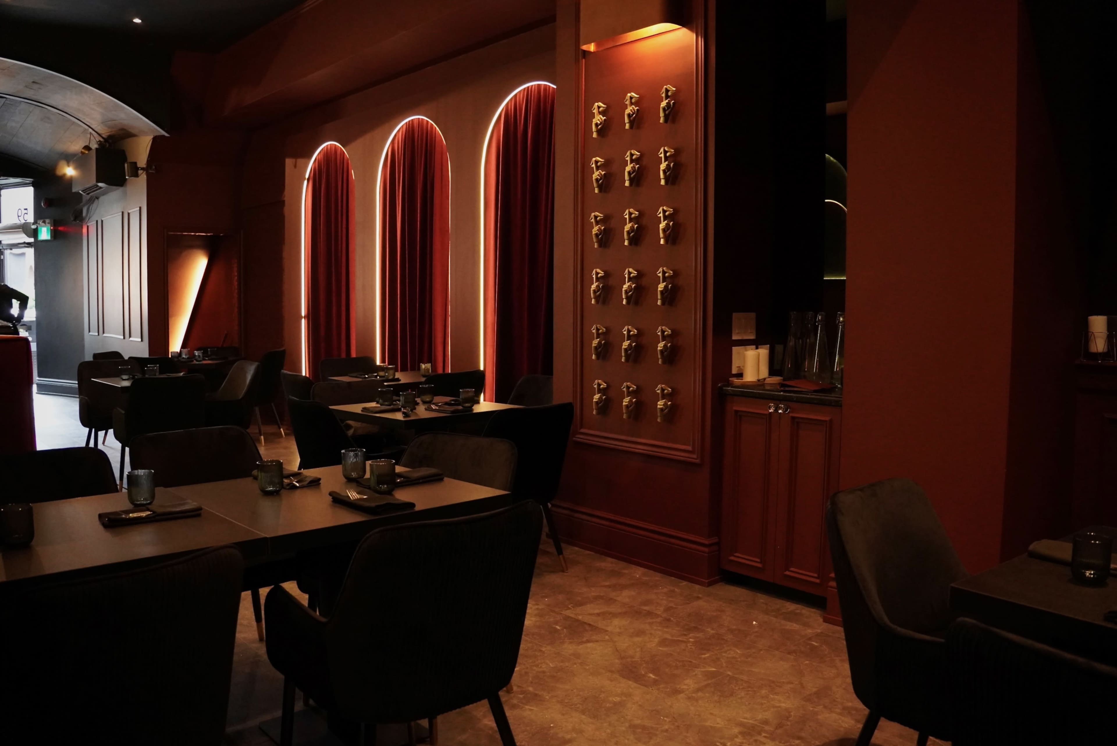The image shows a modern restaurant interior with dark furniture, red velvet curtains, and a wall featuring decorative elements.