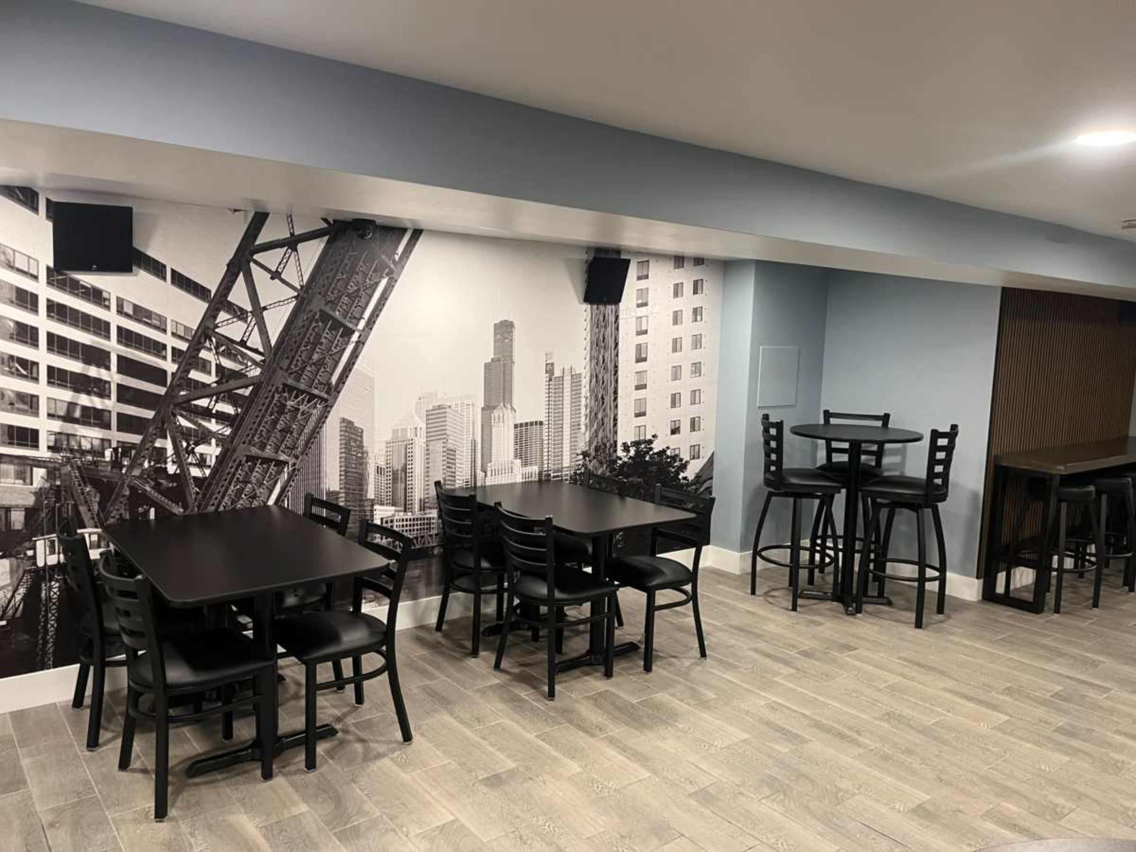 The image shows a modern dining area featuring black furniture and a large black-and-white mural of a city skyline on the wall.