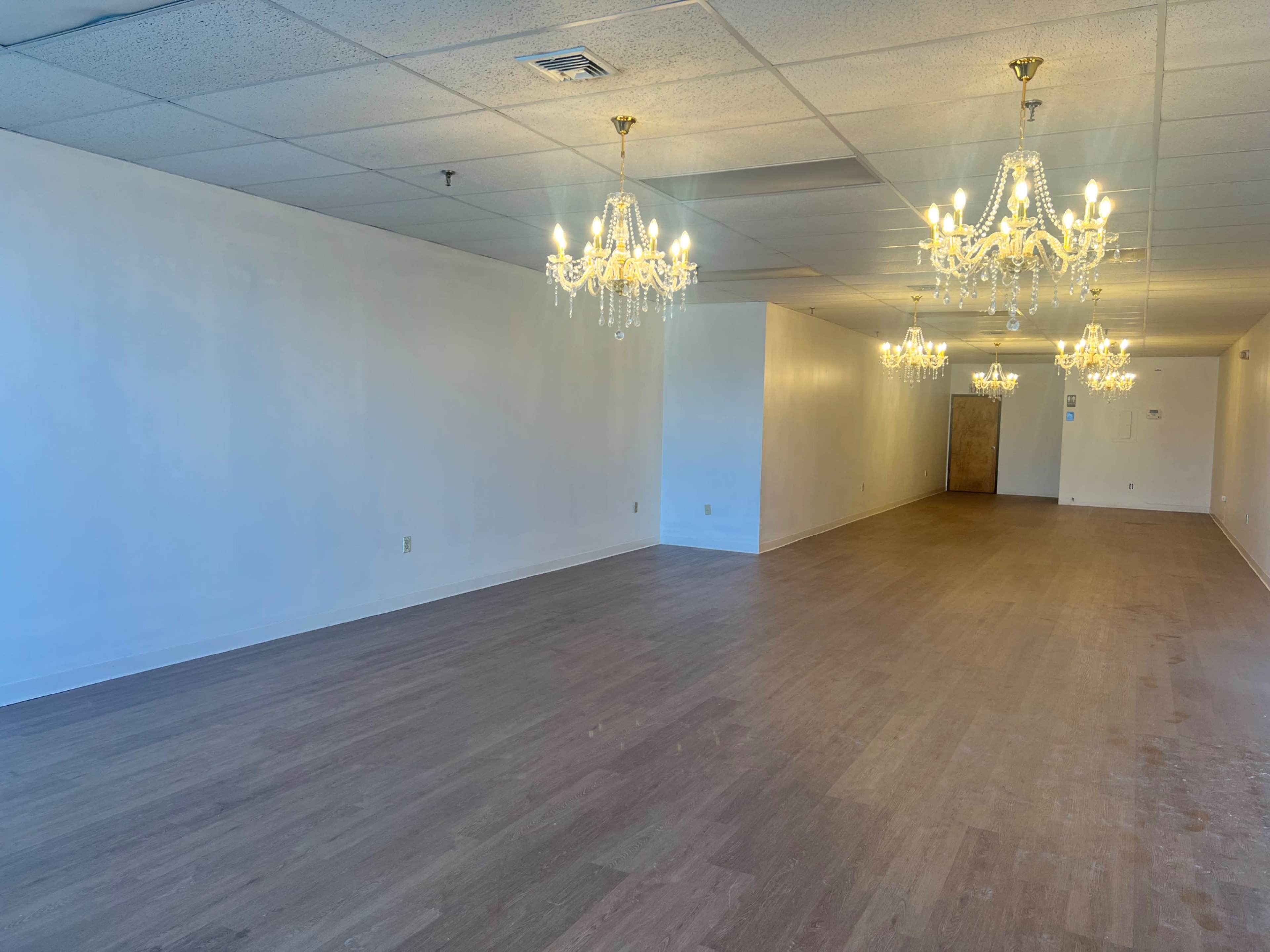 The image shows an empty room with a hardwood floor and several ornate chandeliers hanging from the ceiling.