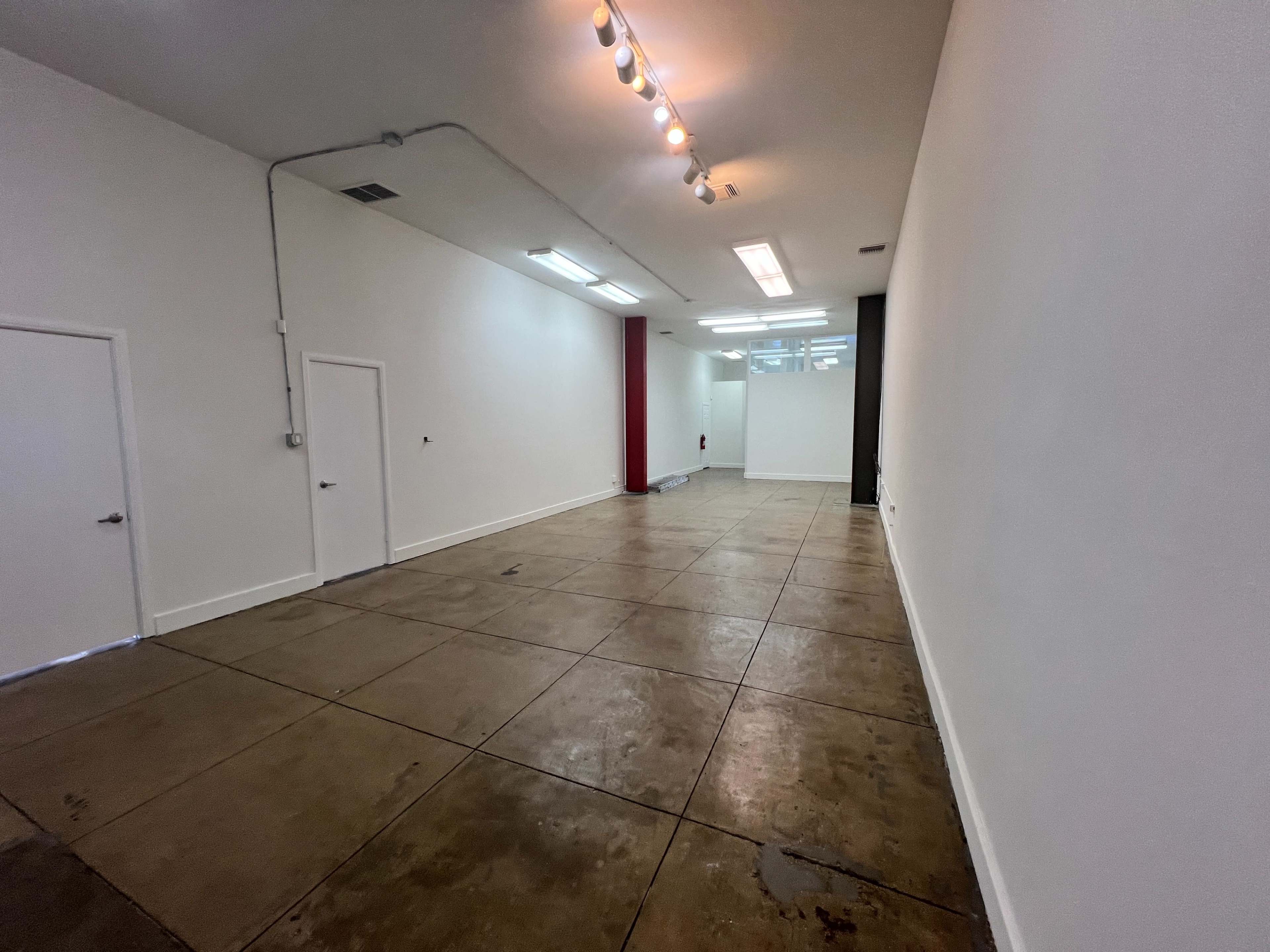 The image shows a spacious, empty room with a polished concrete floor, plain white walls, and two doors on one side.